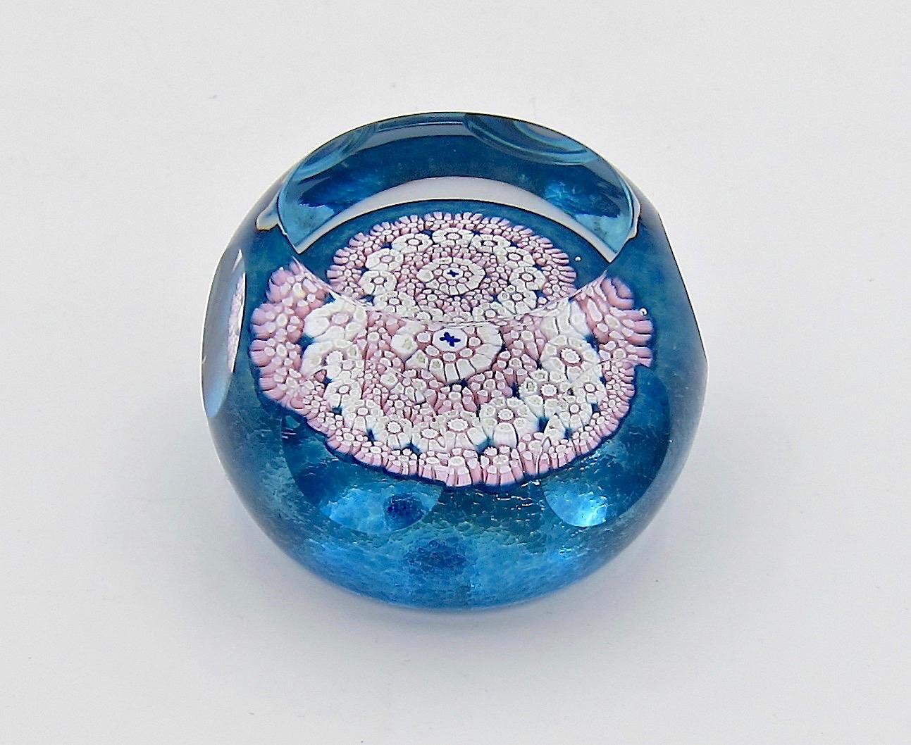 An English art glass paperweight, handcrafted in 1983 by Whitefriars Glass of London. Designed with concentric circles of millefiori canes in pastel pink and white with hints of green surrounding a central butterfly cane of cobalt blue on white. The