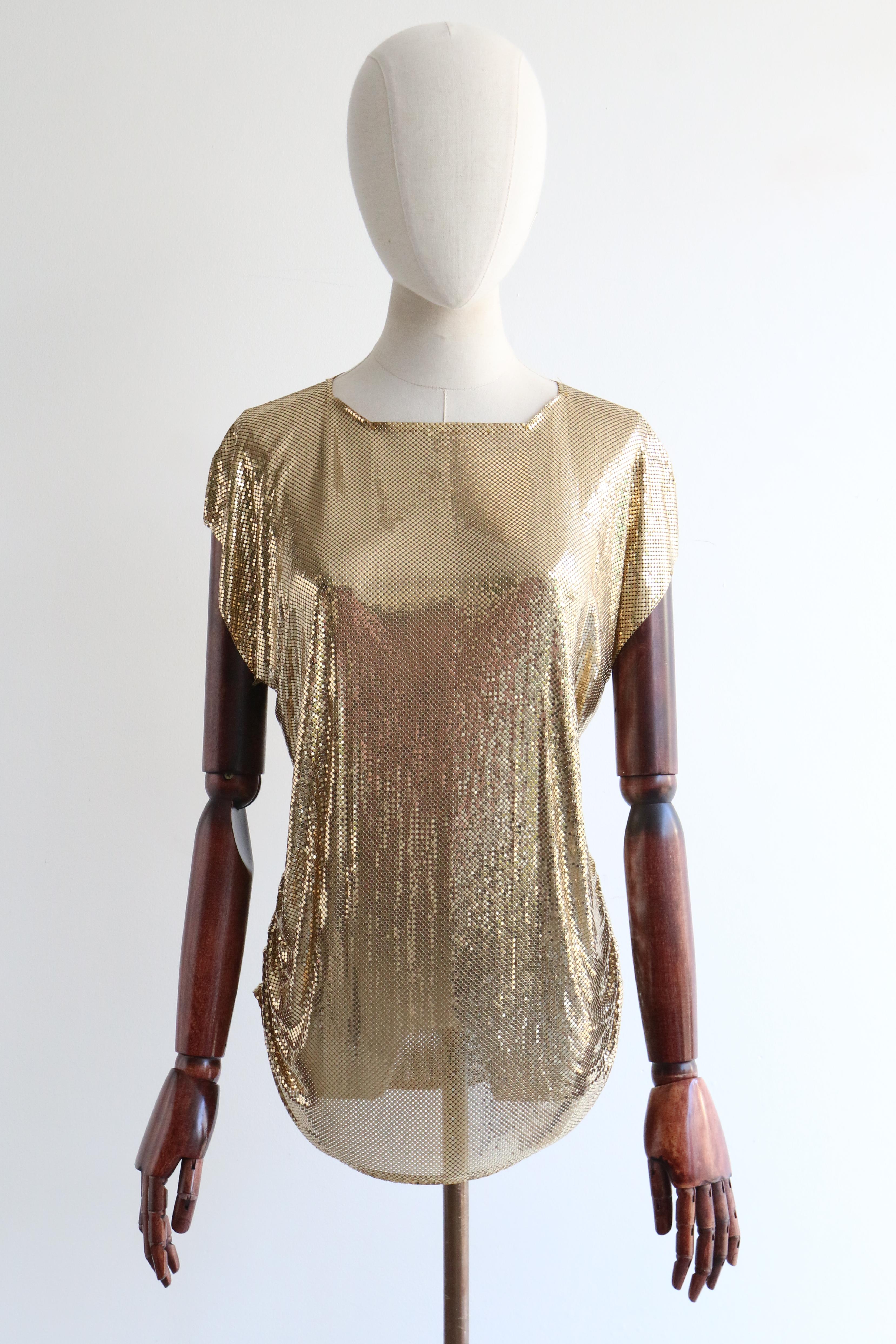 Diese glamouröse goldene Netzbluse von Whiting & Davis aus den 1980er Jahren ist das perfekte Stück Modegeschichte für Ihre Cocktailgarderobe. 

Der eckige, quadratische Ausschnitt ist mit einem Schrägband eingefasst und wird von einer einfachen
