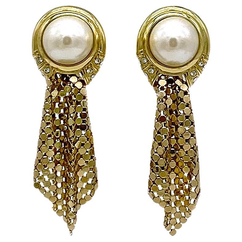 Si tratta di un paio di orecchini a goccia in maglia e perle di Whiting & Davis. Questi orecchini a clip in tonalità oro in stile Art Decor sono caratterizzati da grandi perle simulate decorate con strass chiari e maglie dorate.

La nostra