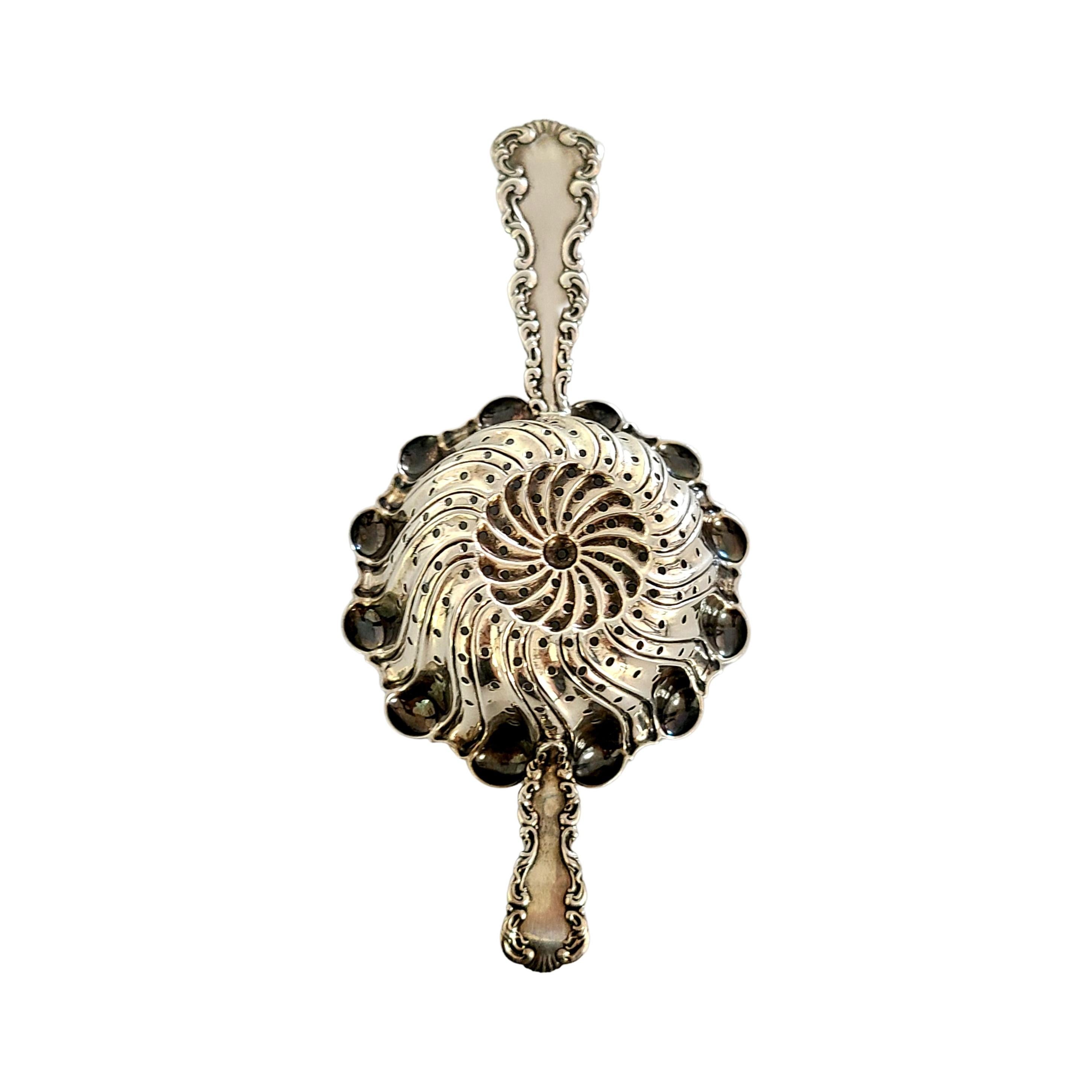 Sterling silver over the cup tea strainer in the Louis XV pattern, by Whiting Mfg Co, circa 1891.

Monogram appears to be S.

Louis XV pattern was designed by Charles Osborne in 1891. It features a flourish design on the handles around a pierced