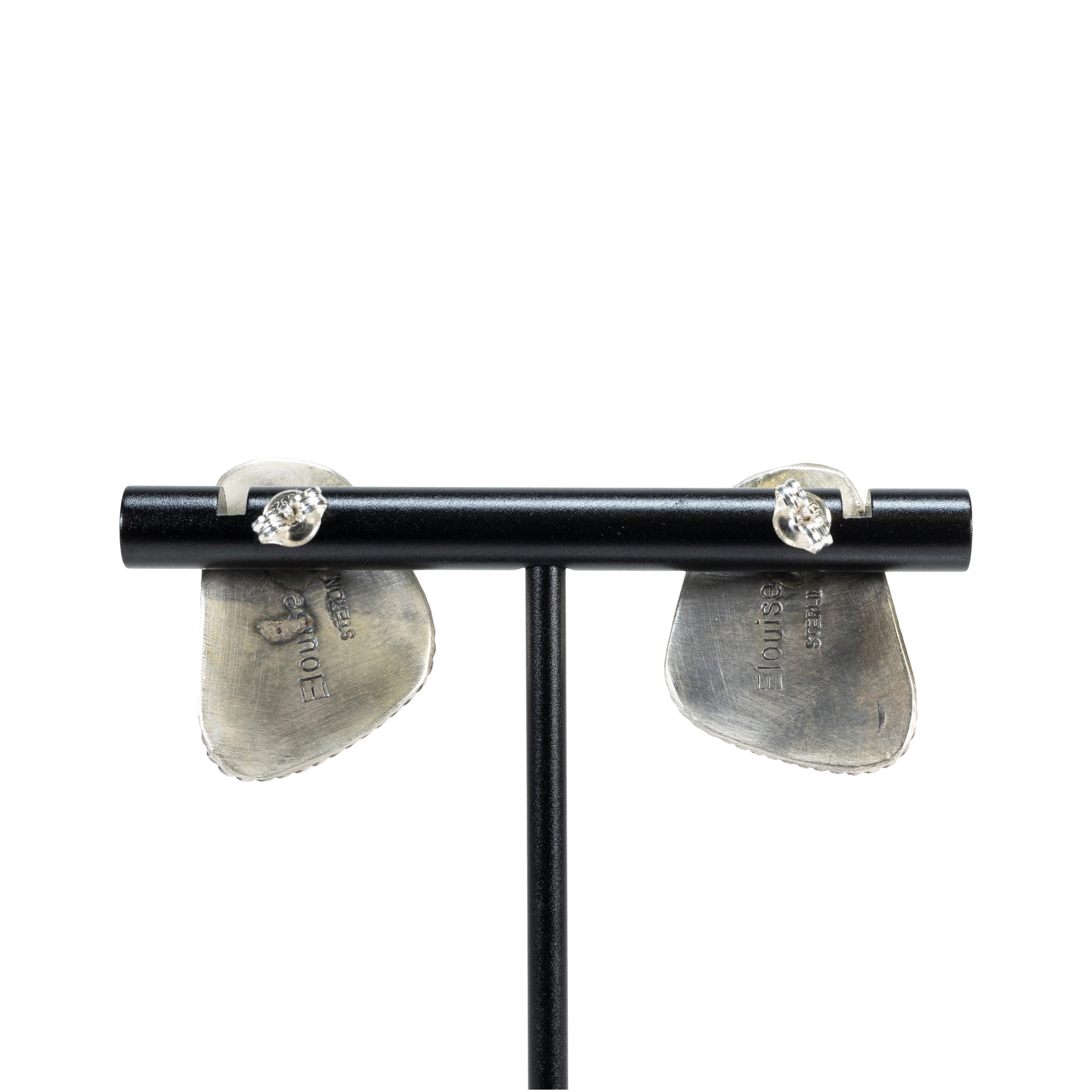 Orecchini a perno in turchese di bufalo bianco Navajo e argento sterling. Le pietre sono tagliate in forma asimmetrica con una colorazione bianca e una matrice nera minima che si concentra soprattutto nella parte inferiore degli orecchini.