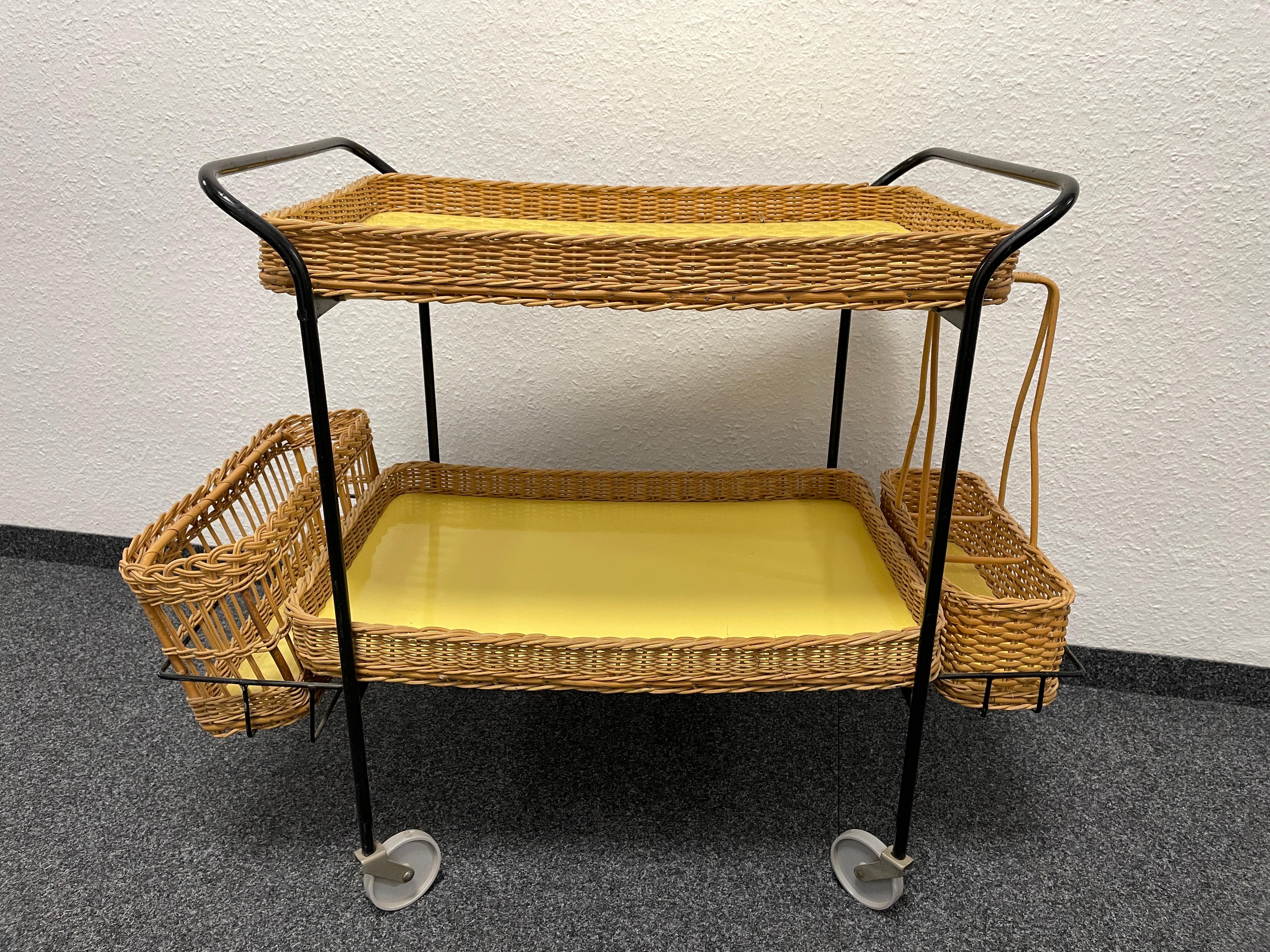 Striking mid-20th century bar trolley in metal with hand-woven wood and wicker fittings. Wood and wicker drink tray on top and on the bottom. Also included a bottle basket carrier and a bottle holder. Nice addition to your home, patio or garden.