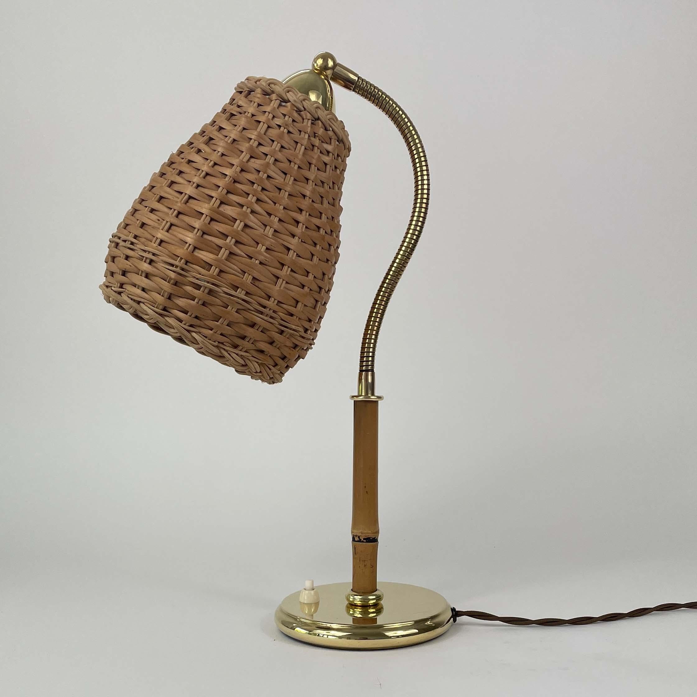 Esta lámpara de mesa vintage fue diseñada y fabricada en Austria en la década de 1950. 

La lámpara tiene una base de latón, un tallo de bambú y una pantalla cilíndrica de mimbre tejido. El mimbre es de color marrón claro natural y tiene un acabado
