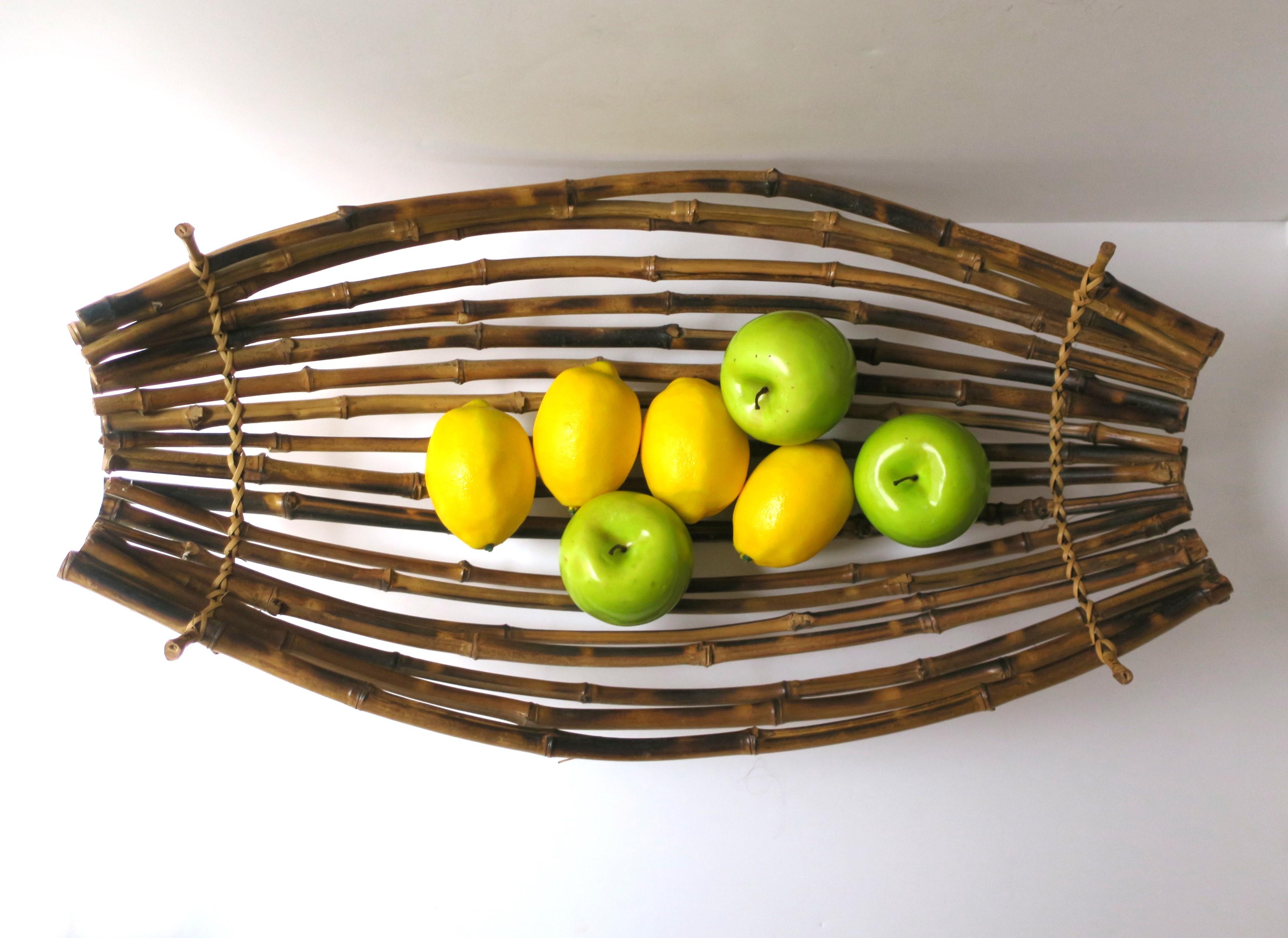 A wicker bamboo oblong centerpiece basket, circa late-20th century. Basket is all bamboo with wicker wrapped ends. Piece can hold fruit (demonstrated), vegetables, bread, etc. Great a centerpiece basket on a dining table, credenza, etc., indoors or