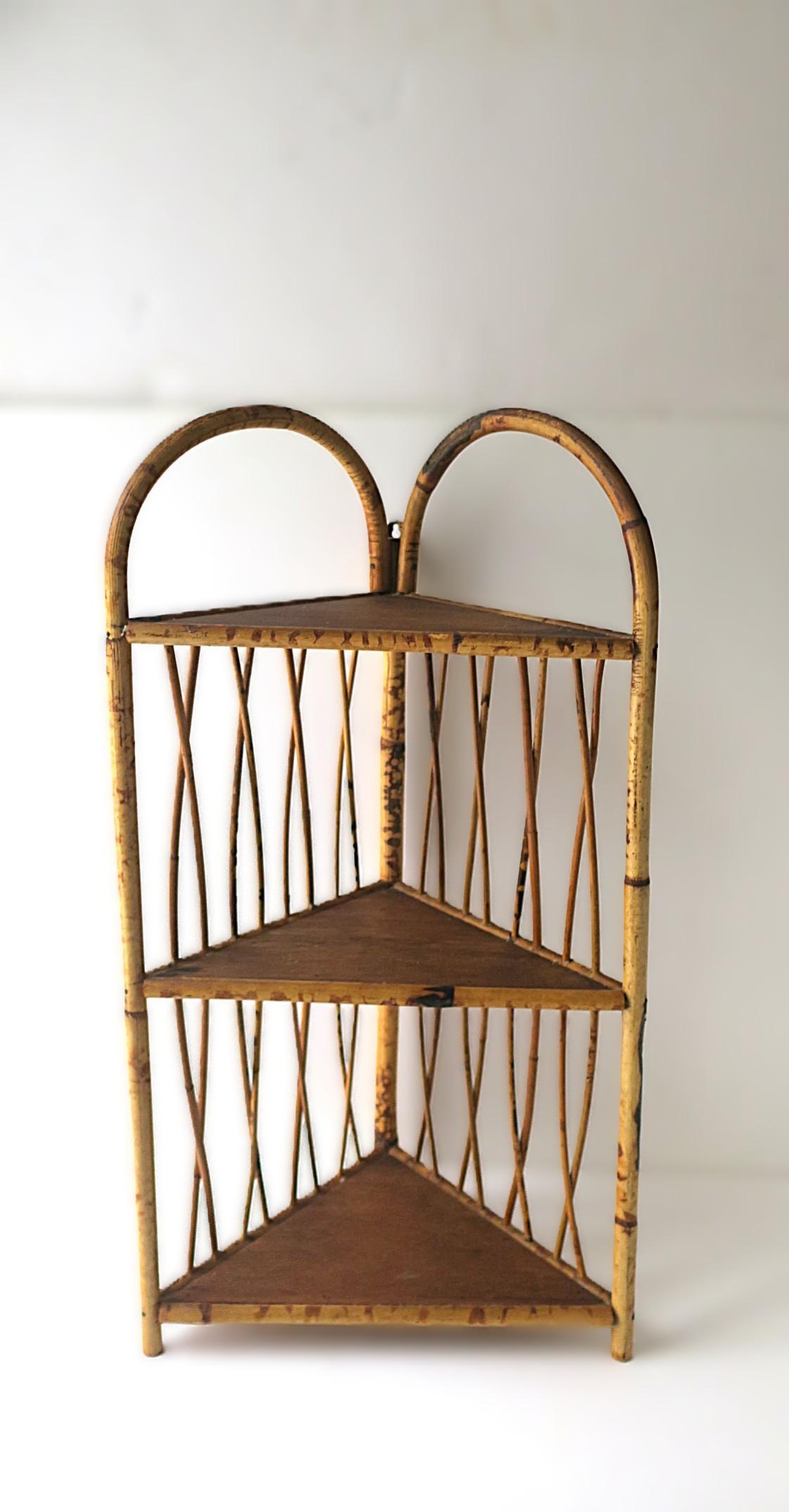 Ein Bambus-Eckregal aus Weidengeflecht für die Wand oder den Boden. Das Stück hat drei (3) Ablageflächen mit kreuz und quer verlaufenden, gitterartigen Seiten. Aufhängen oder auf Bodenhöhe verwenden. Wandhaken aus Messing an der Rückseite zur