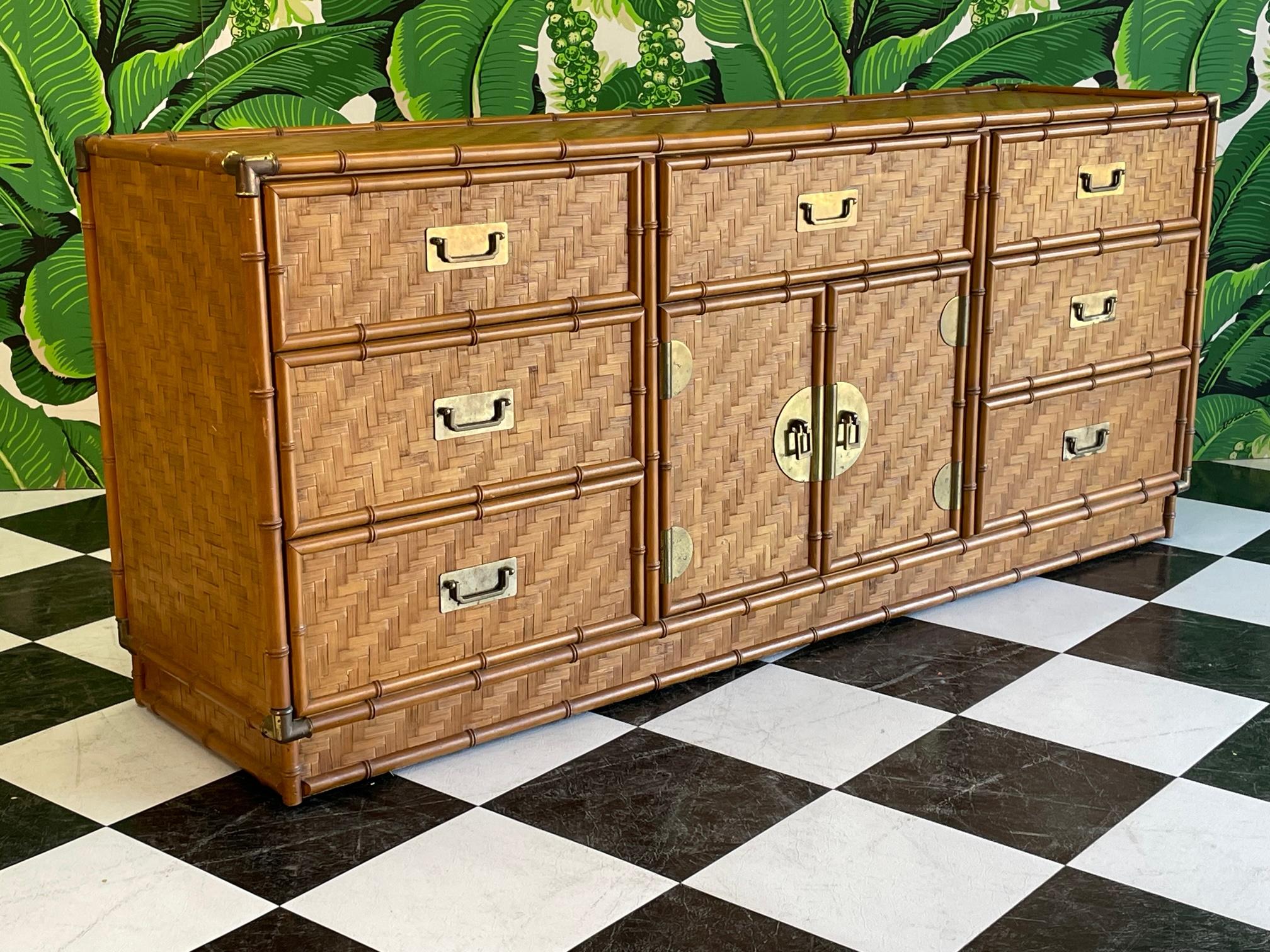 Vintage campaign style 9-drawer dresser features faux bamboo detailing and a complete veneer of woven rattan basket weave in a herringbone pattern. Brass hardware and corner accents. The unique rattan veneer gives a look of parquet. Warm, rich tone
