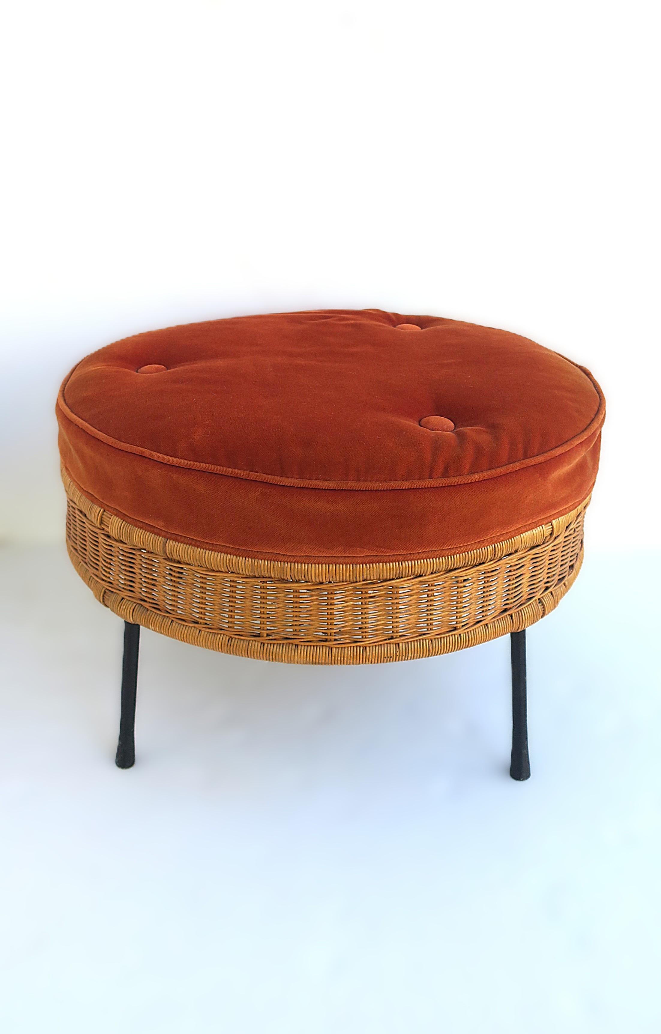 Pouf rotondo in vimini con cuscino imbottito arancio-bruciato e base in ferro annerito. L'ottomana o sgabello ha una base in ferro nero con quattro gambe, un rivestimento esterno in vimini marrone, rifinito con un cuscino per la seduta leggermente