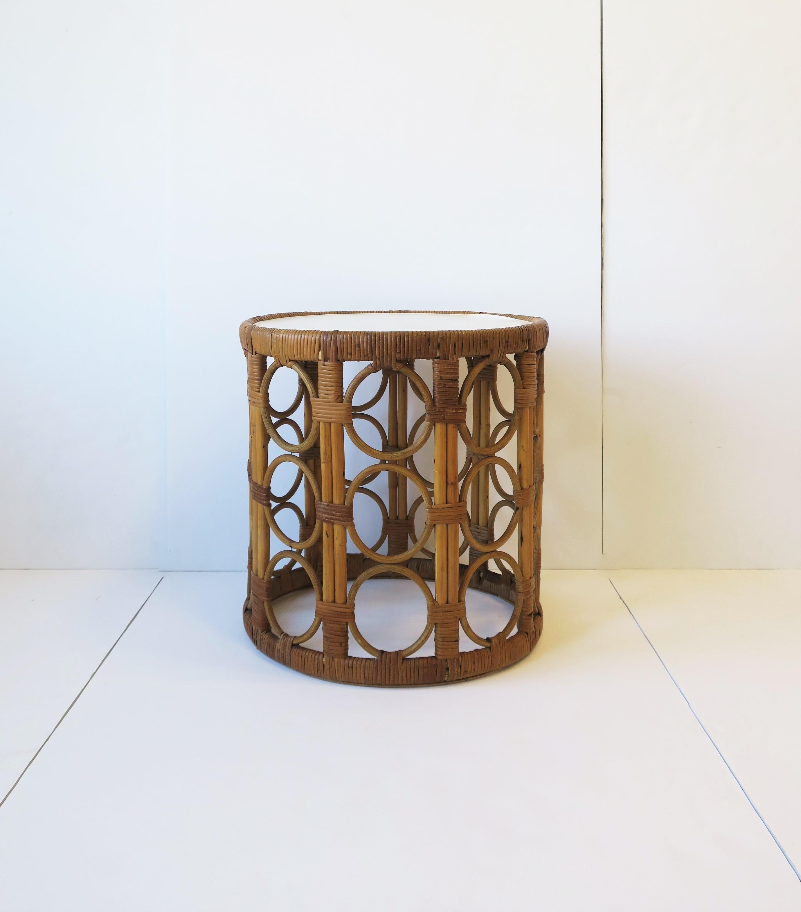 A round vintage wicker side or end table with circle-loop design, circa mid-20th century, 1960s. A round wicker end or side table with loop/circle designed base frame, finished with an attached white laminate top with wicker edge. 

Dimensions: