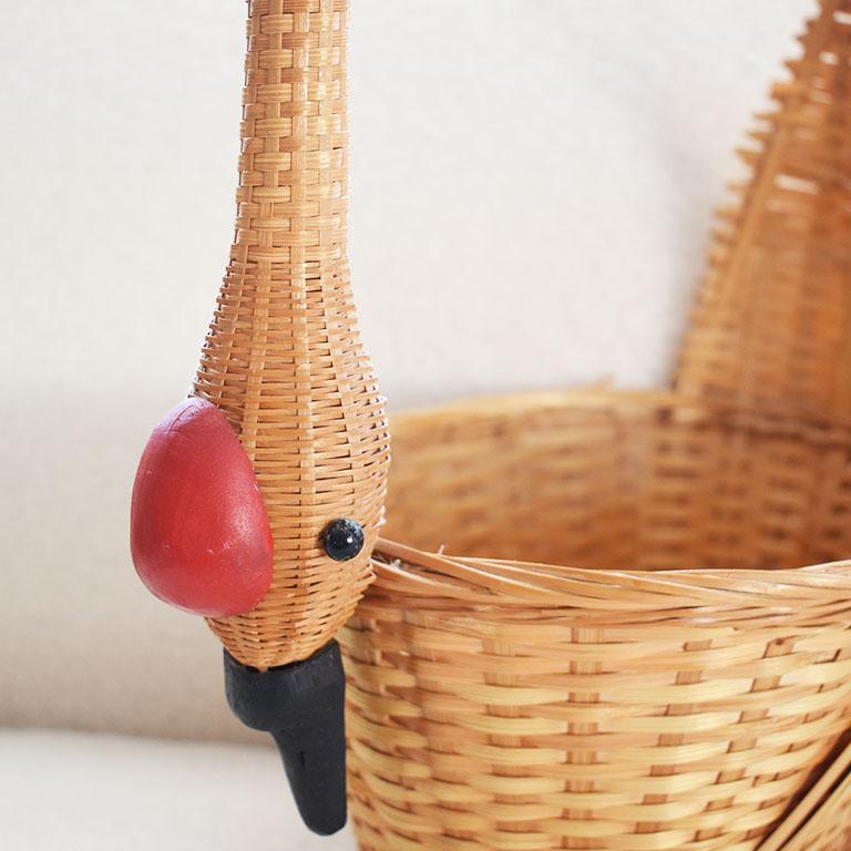 A vintage wicker duck motif basket with a tall handle. This whimsical basket features a handle woven with a wooden duck or swan head with a red top, black wooden eyes, and beak. 

Dimensions:
12