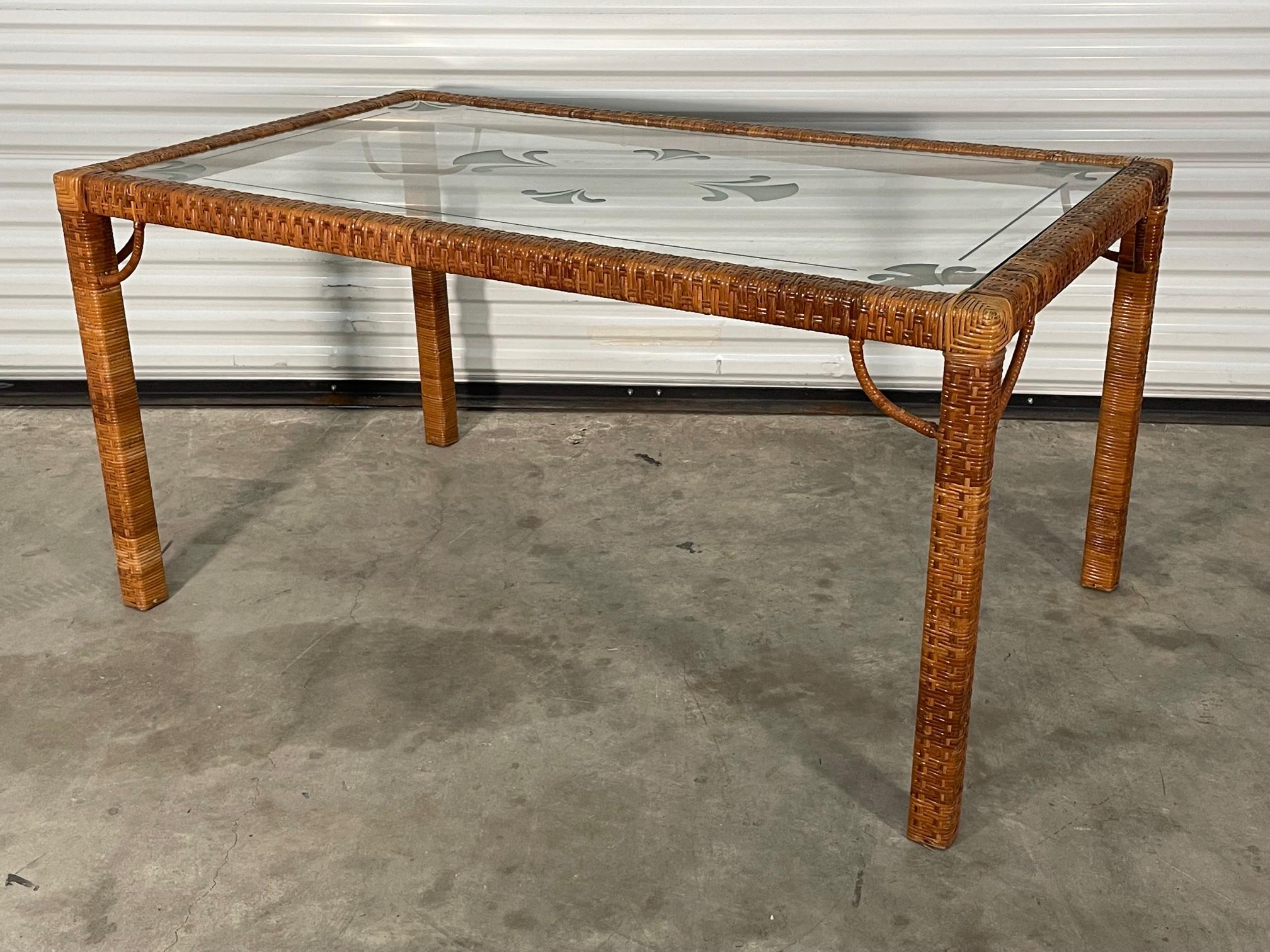 Vintage dining table features a full wicker wrap in a basketweave style. Glass top features etched designs with a modern take on the fleur-de-lis. Good condition with imperfections consistent with age. May exhibit scuffs, marks, or wear, see photos
