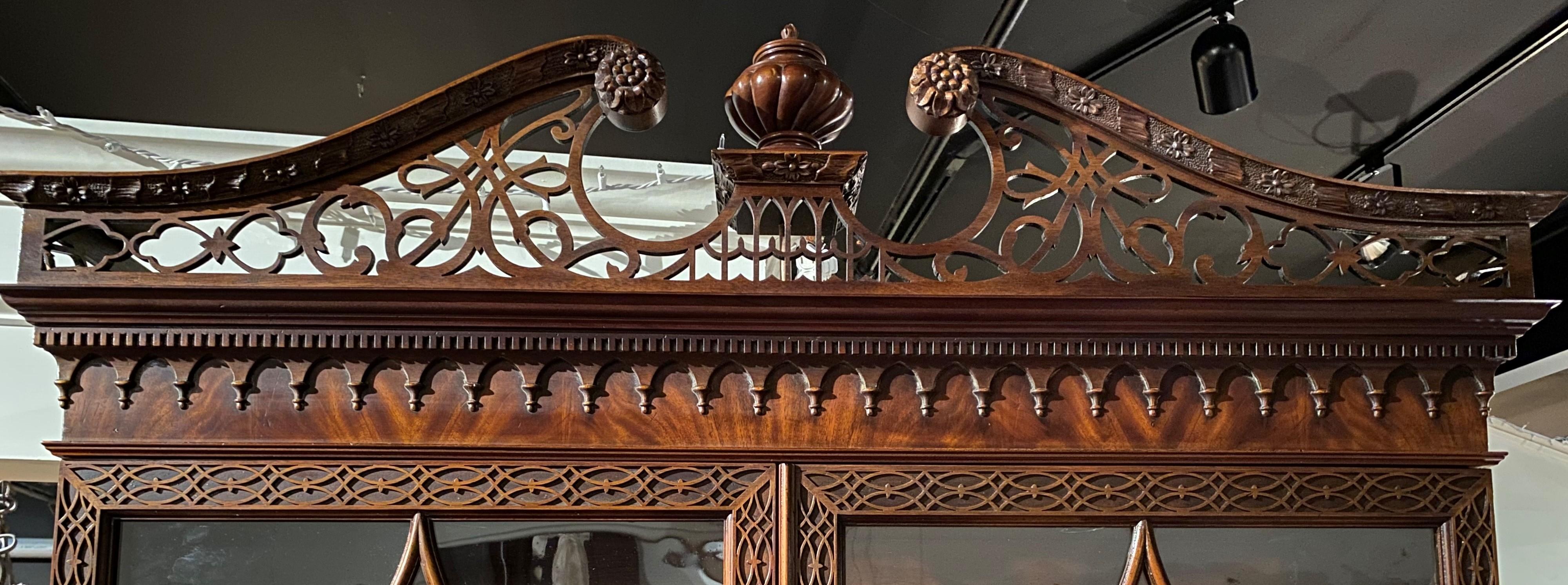 A fine Chinese Chippendale style two-piece mahogany lighted display cabinet with fitted butler’s desk by John Widdicomb Co, Grand Rapids, Michigan, featuring a beautifully carved reticulated split pediment with a center elevated urn form finial