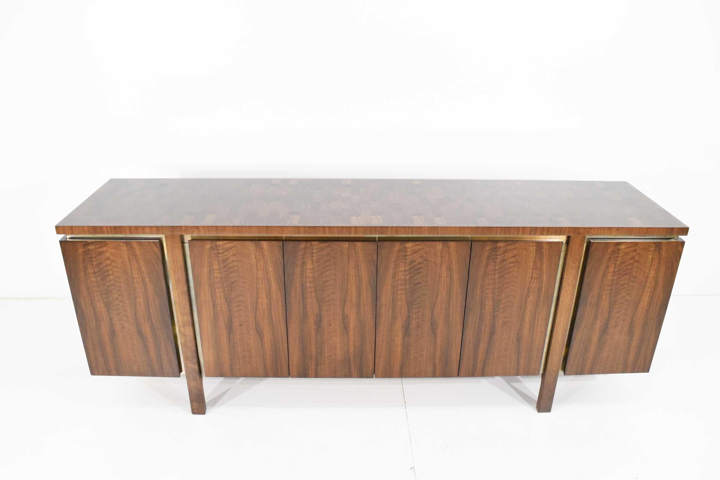 A beautifully restored credenza by John Widdicomb in walnut. The credenza has four doors with a brass reveal behind the doors. Legs give the effect of floating.