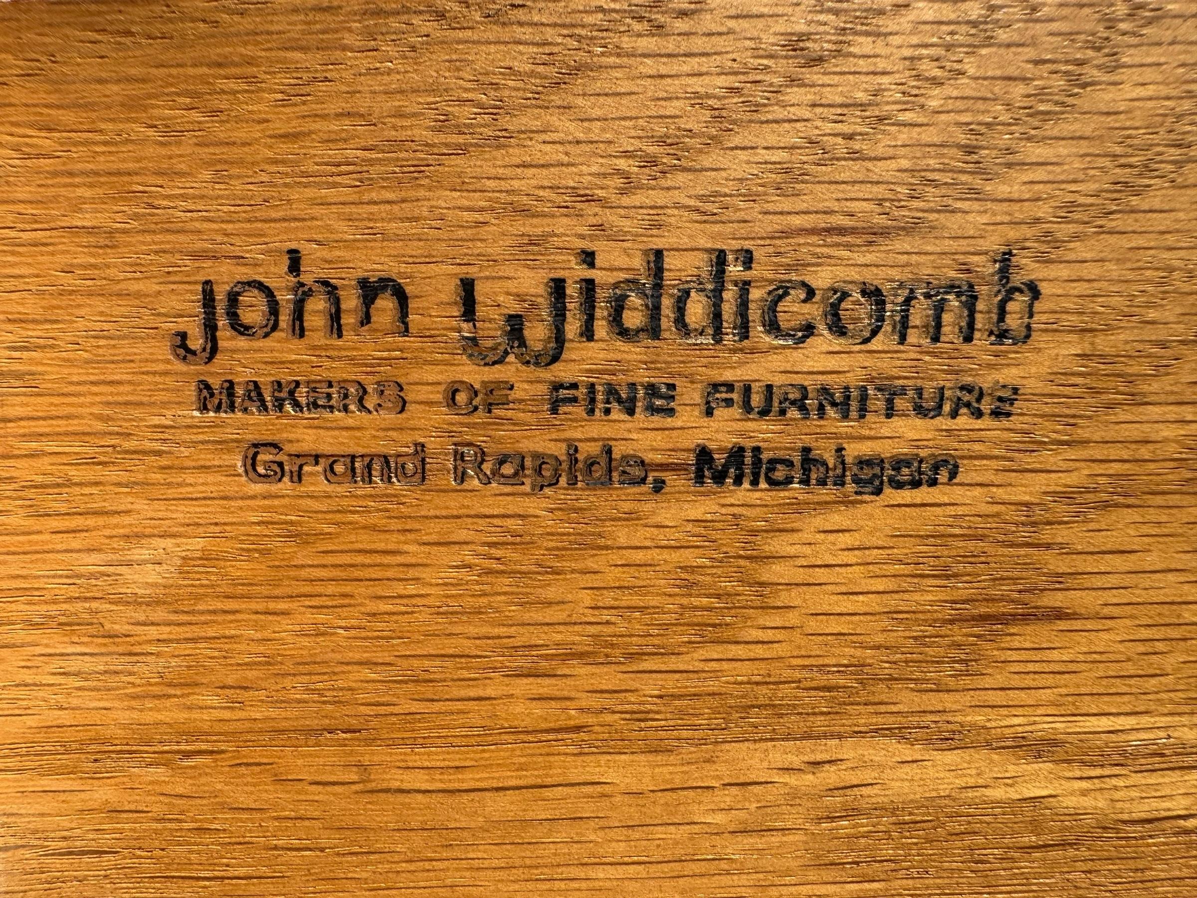 A John Widdicomb mid-century period credenza in walnut. Carved and gilded in front, three central drawers and cabinets at either side open with original hardware. Finished with bun feet.