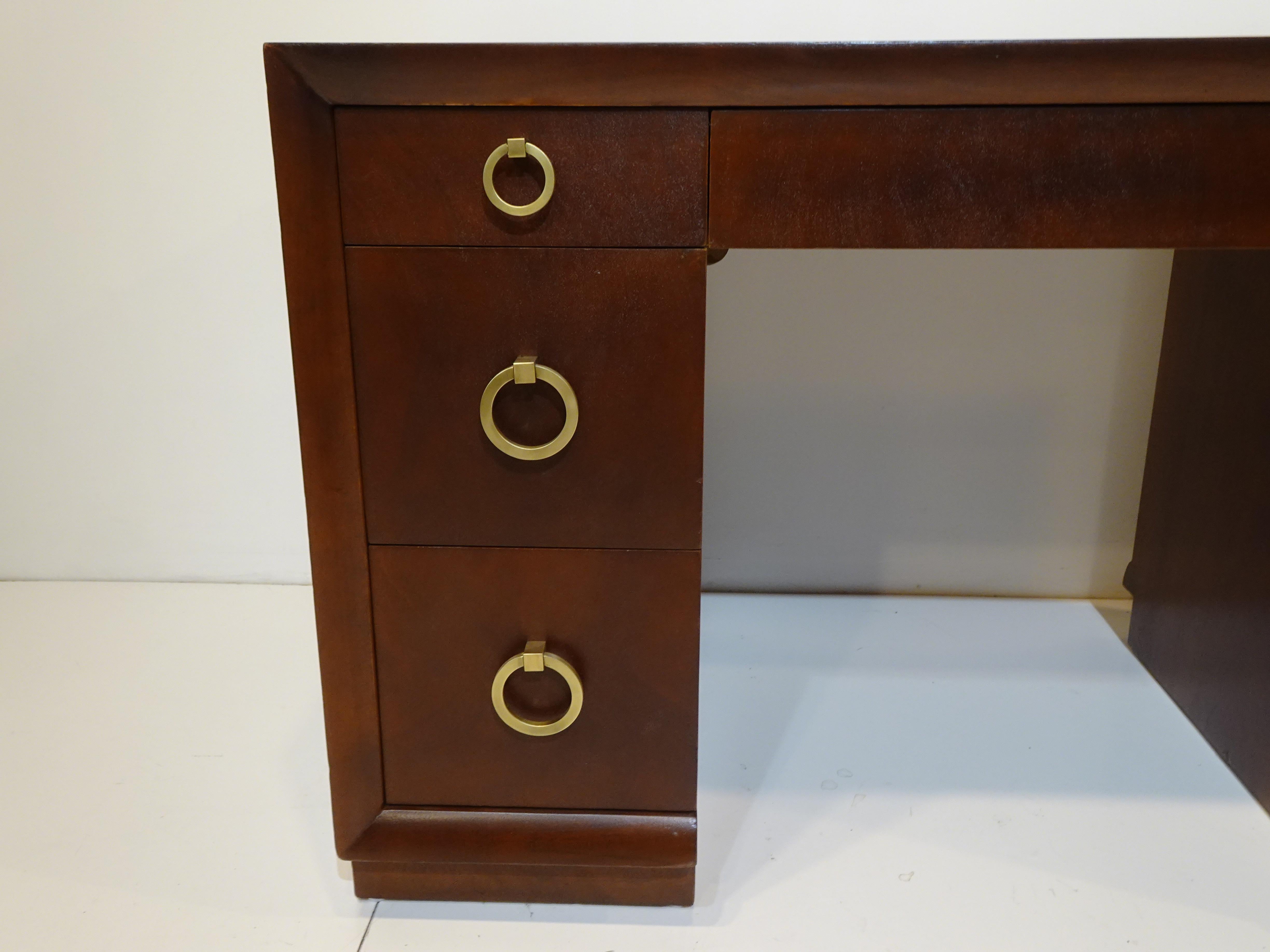 A very well crafted dark mahogany kneehole desk with three drawers to each side and a middle pencil drawer to the top . Solid brass ring pulls to the drawer fronts on each side and the finished back having carved lines to the wood break up the plane