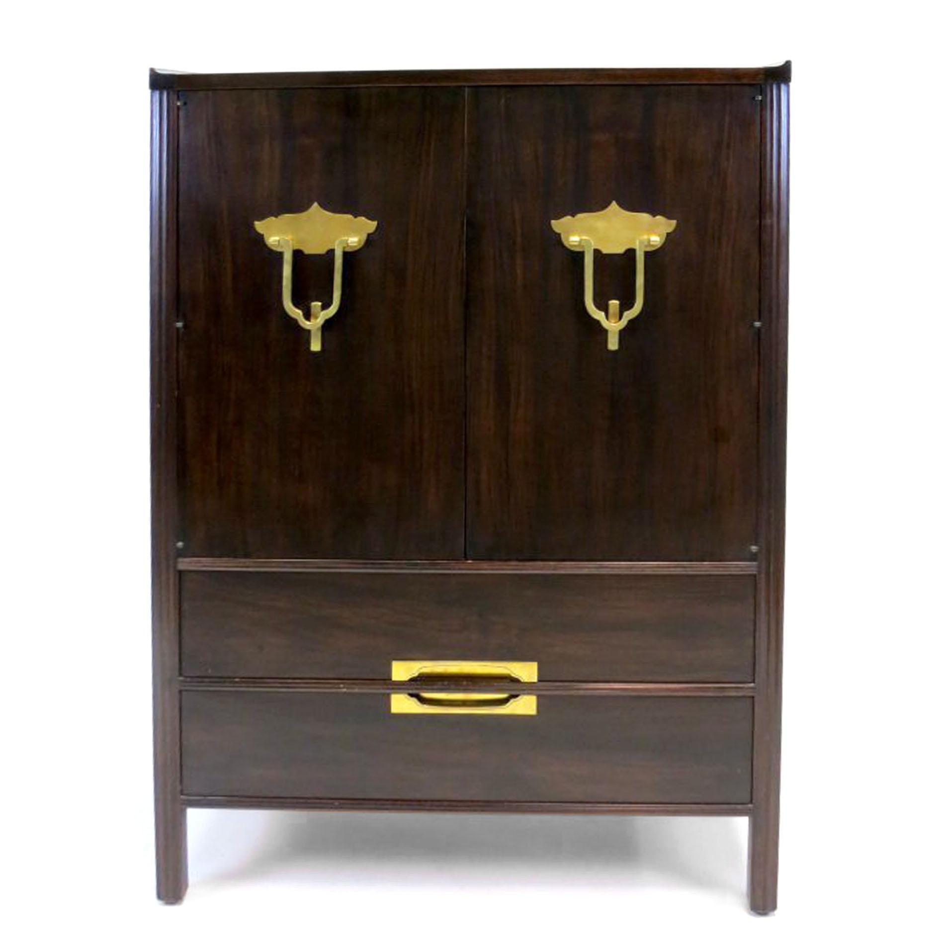 Tall cabinet or small armoire with two doors above two drawers by Widdicomb in an ebonized mahogany finish. Fantastic Asian insprired brass handles and inset pulls on the drawers, with reeded detailing and upswept top edge. Interior has one drawer