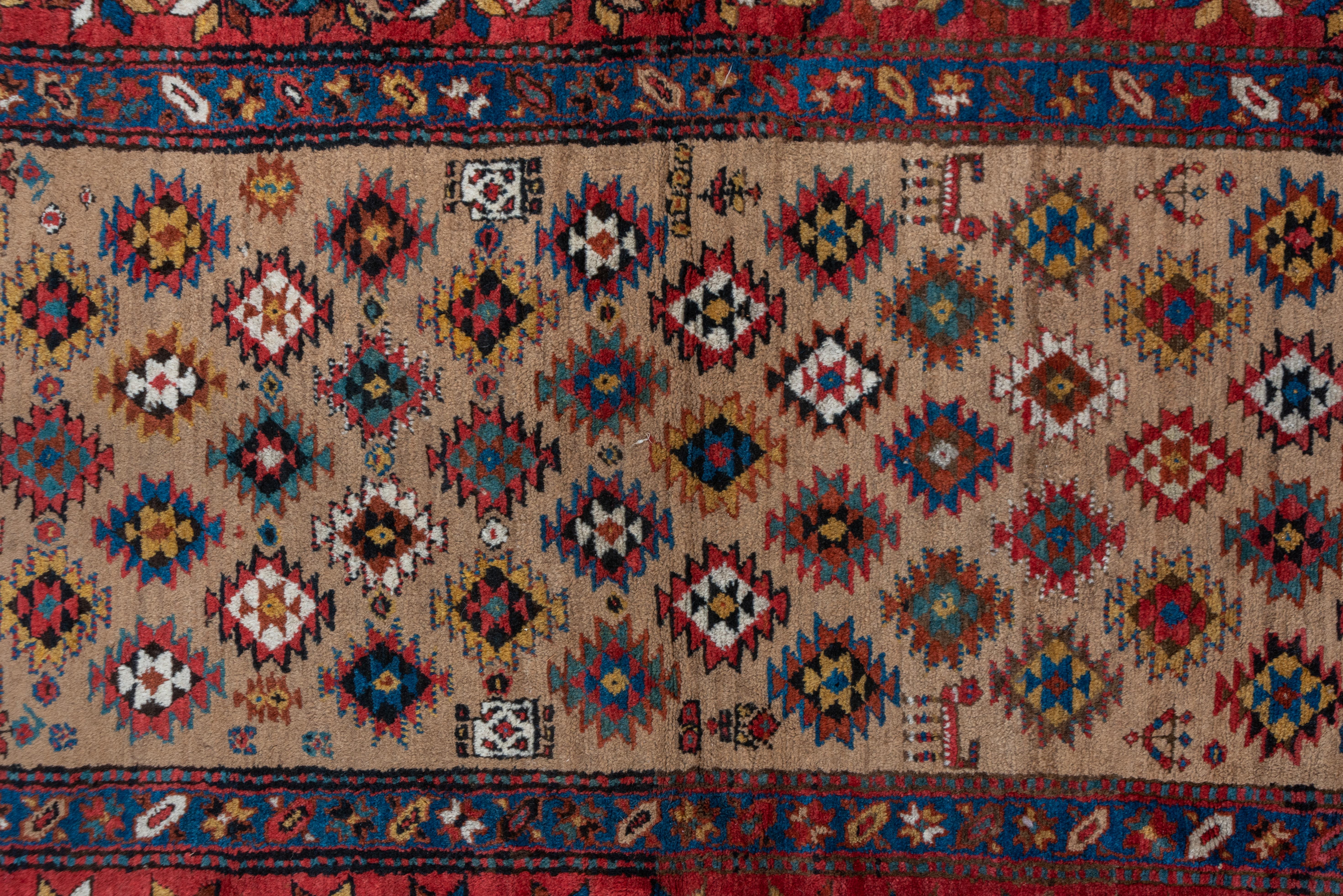 The beige camel ground shows a half-drop offset row pattern of larger and attendant smaller ashiks, along with small animals and flowers, detailed in off-white, medium blue, orange-rust, off black, straw and red. Main red ground border of polychrome