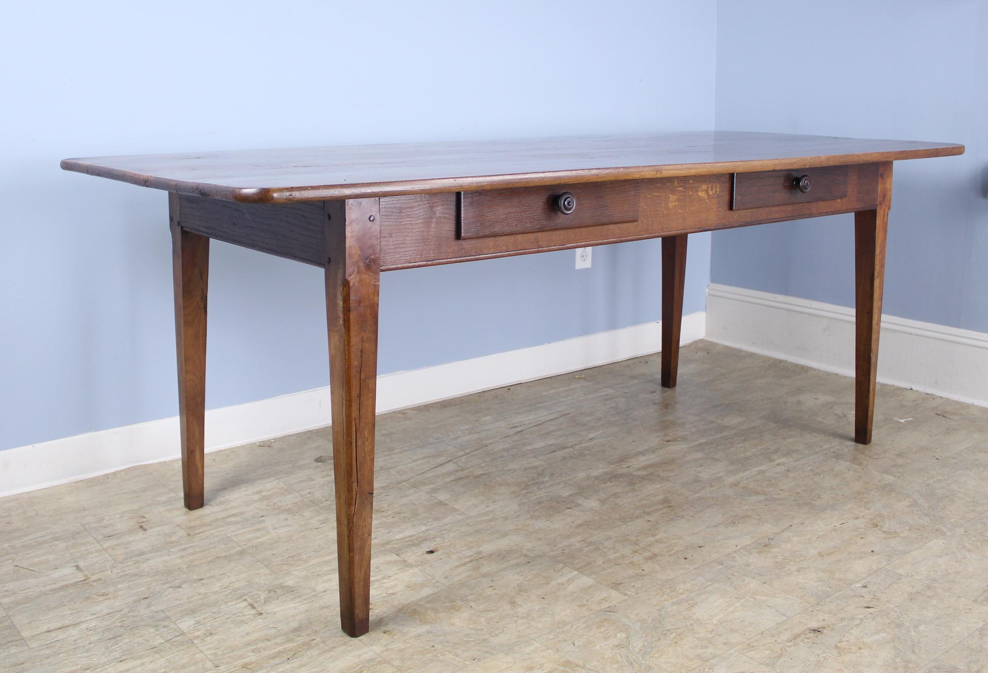 A two-drawer antique farm table with very good depth and wonderful dramatic walnut grain. Nice rounded corners on the tabletop add a modern note. Interesting carved detail at the top of the legs, which are 58.5 inches apart on the long side. 24-inch