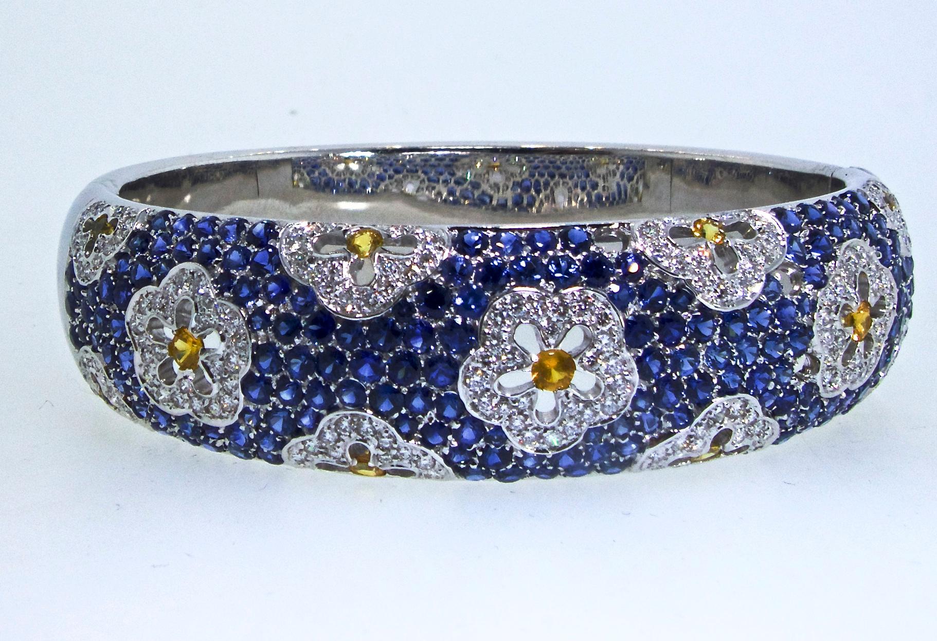 Sapphire and Diamond bracelet with floral motifs on a bed of blue sapphires.  This large 18K white gold bangle bracelet has sturdy, well made, clasp.  It is 7 inches in diameter.  The natural blue sapphires are bright and vivid, the natural yellow