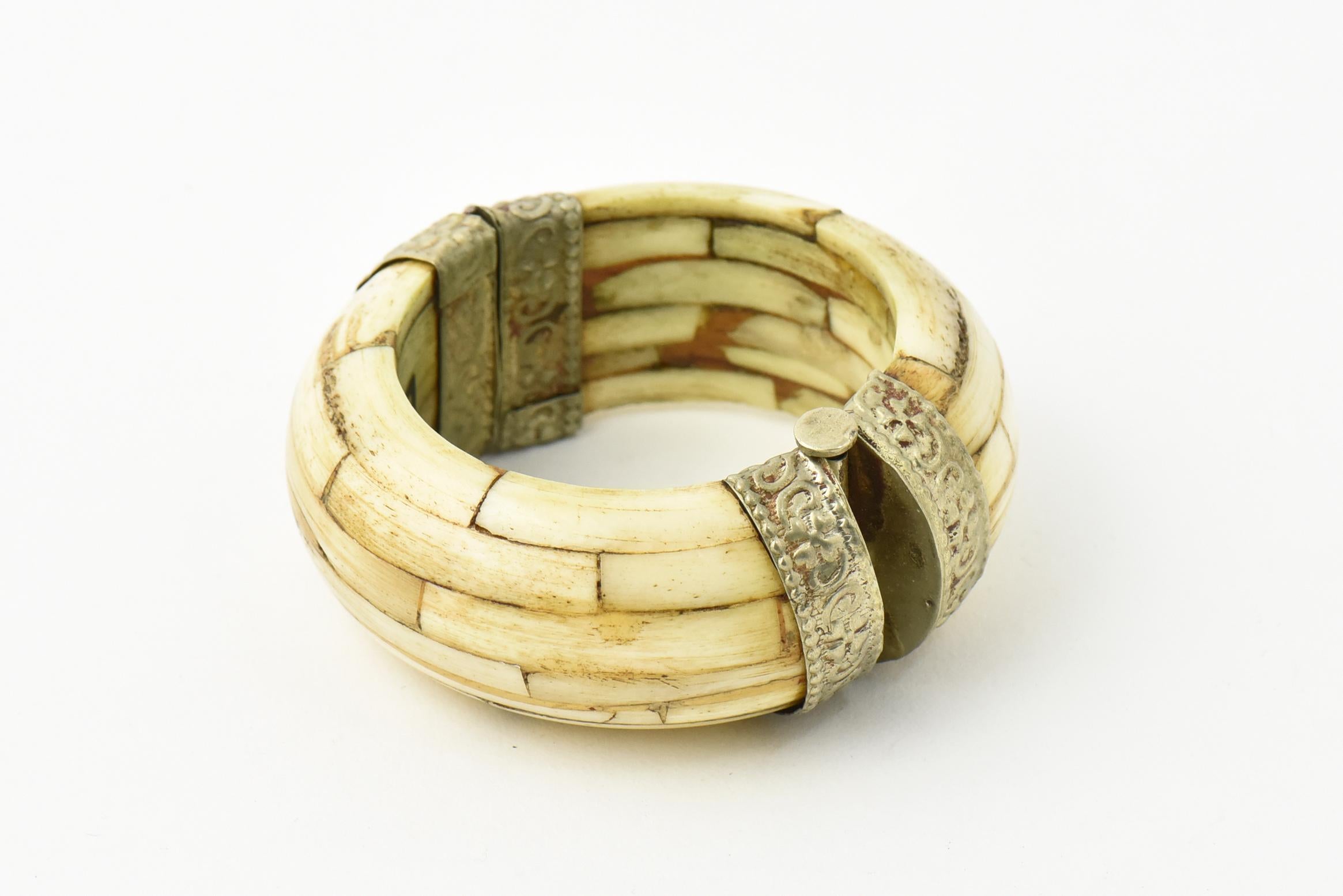 Bone bangle with silver-plated caps with raised floral design on the edges. Handmade in India. Pin closure. Interior, 6.5