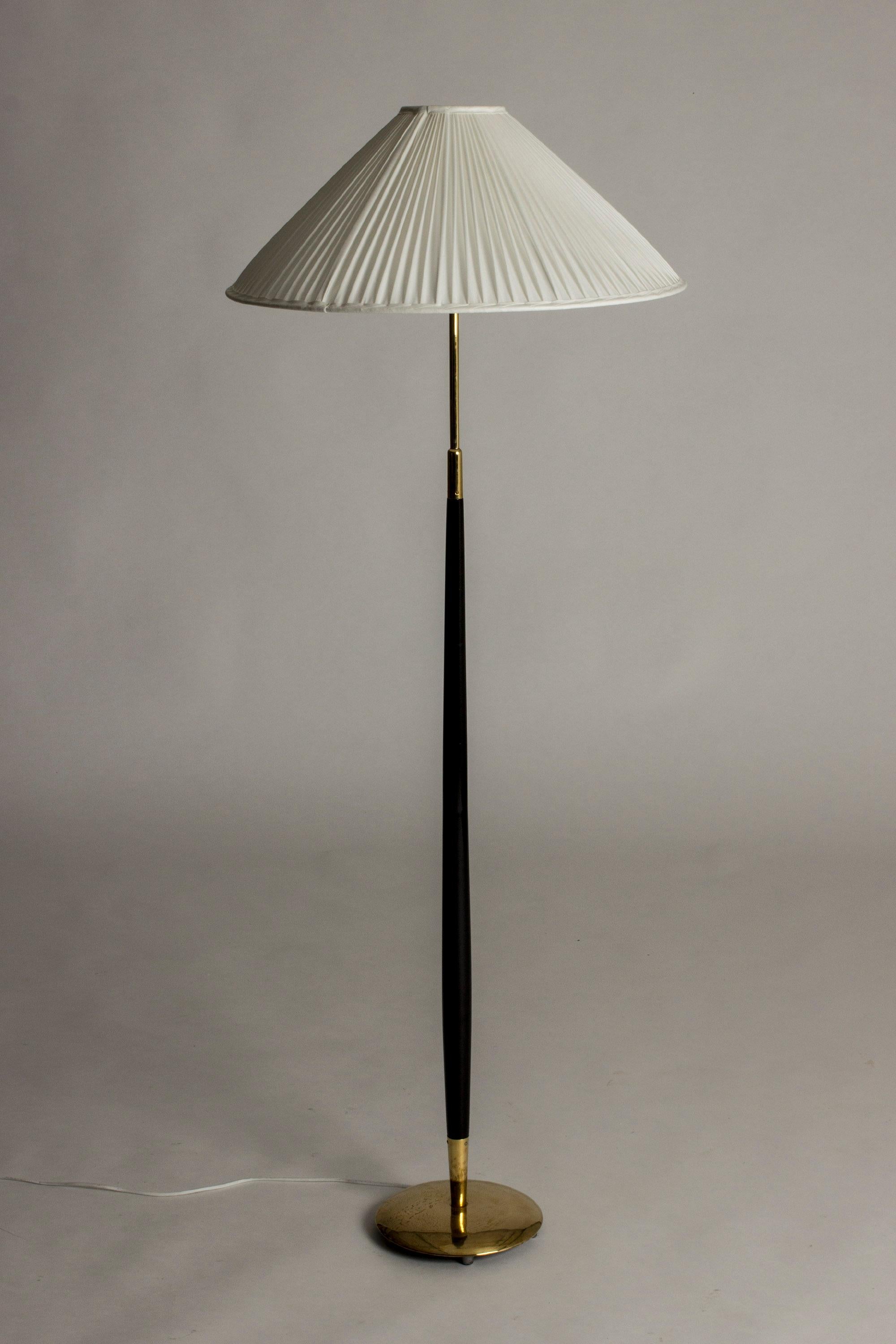 Elegant floor lamp by Bertil Brisborg, with a tapering black lacquered pole and brass base. Beautiful wide shade, made from white pleated fabric.