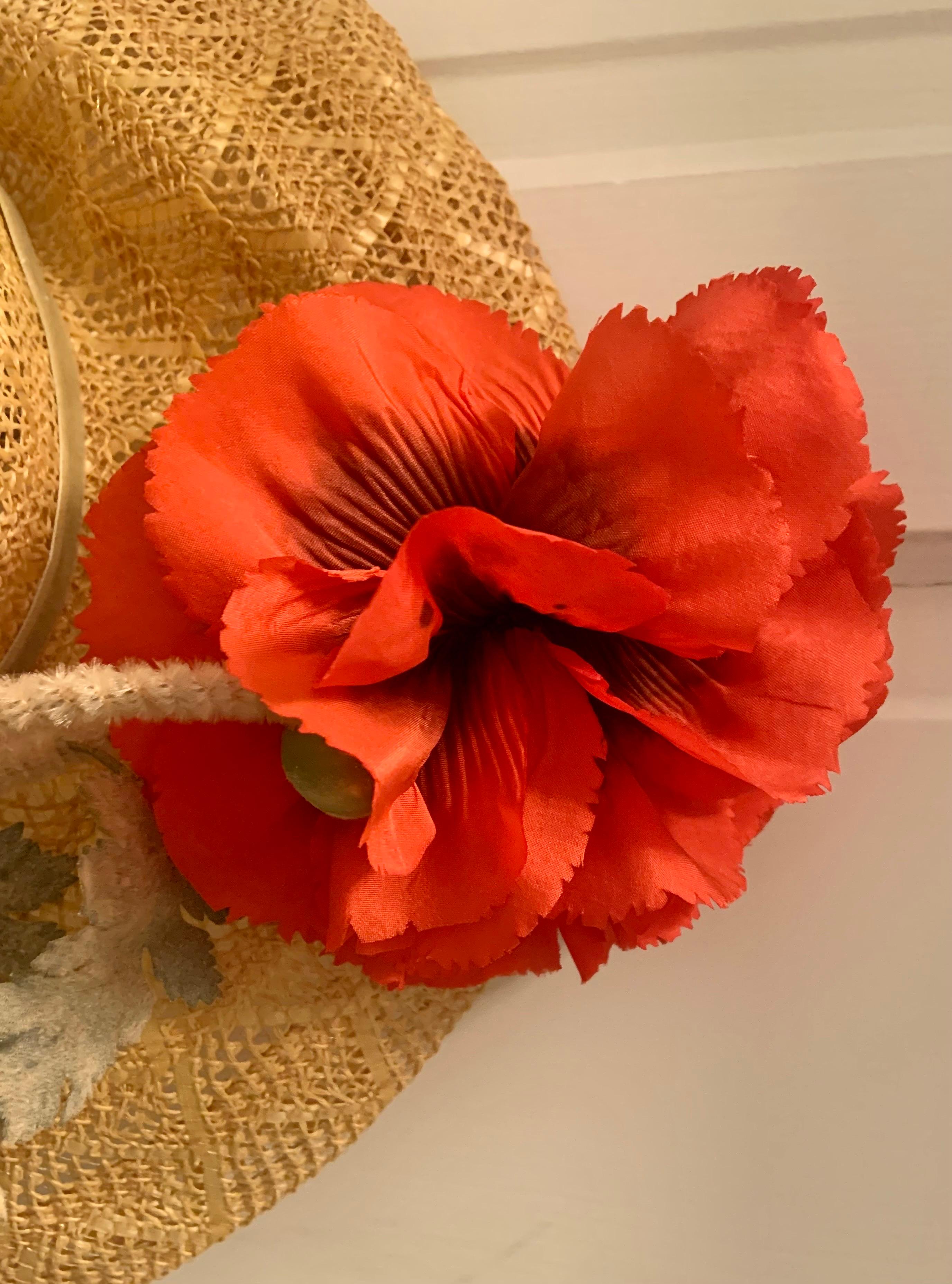 This is a beautiful wide brimmed straw hat with a red silk poppy which looks like it was just picked.  The hat was designed by Jack McConnell in New York. the poppy has two long stems, one for the flower and another for a bud. They are both trimmed