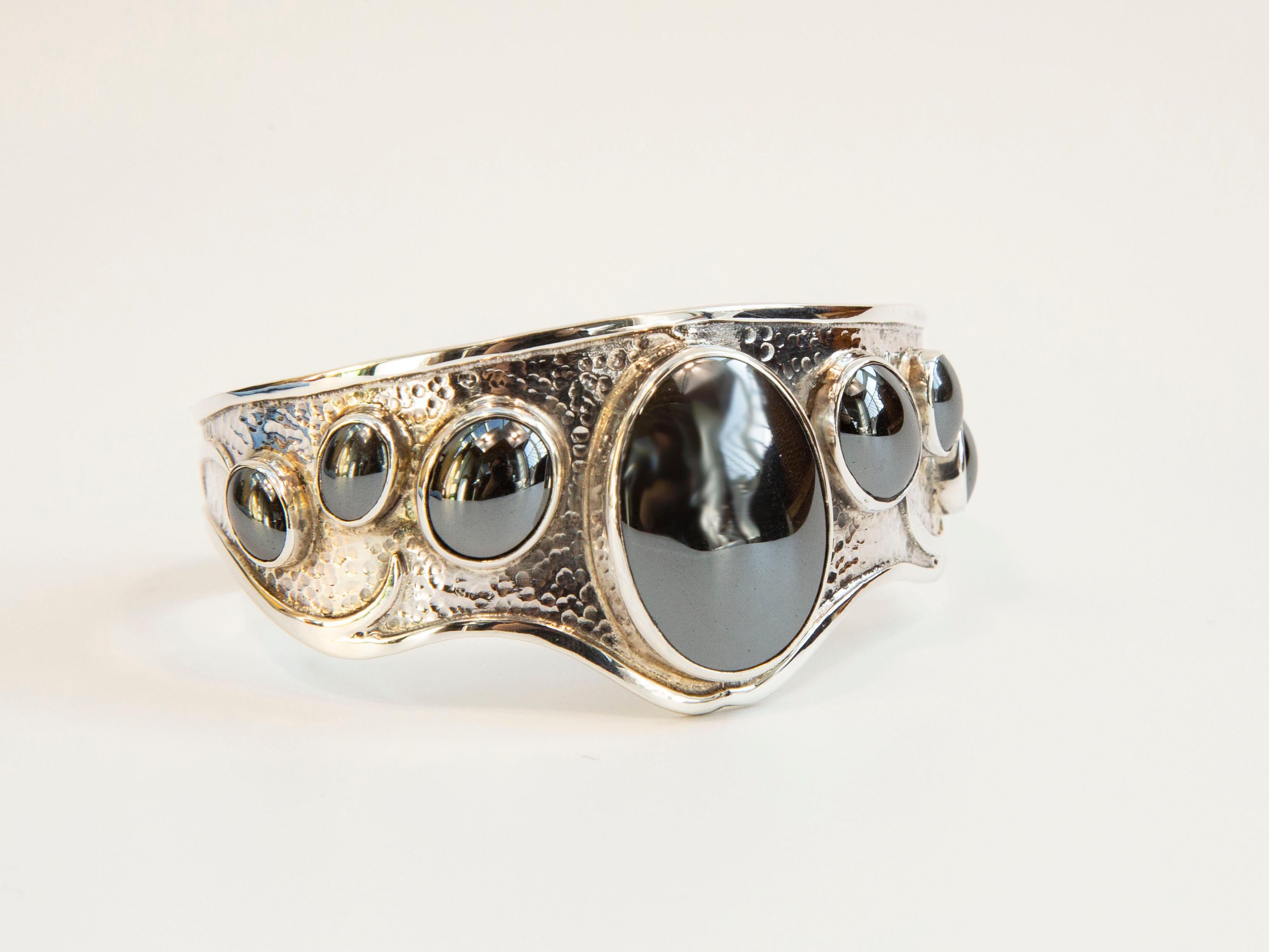 A vintage wide contoured hammered cuff  bracelet with 7 oval hematite cabochons. The bracelet is marked 925 that stands for 0.925 silver content = sterling silver. The bracelet weights 30 grams. The bracelet is 6 cm in diameter (measured