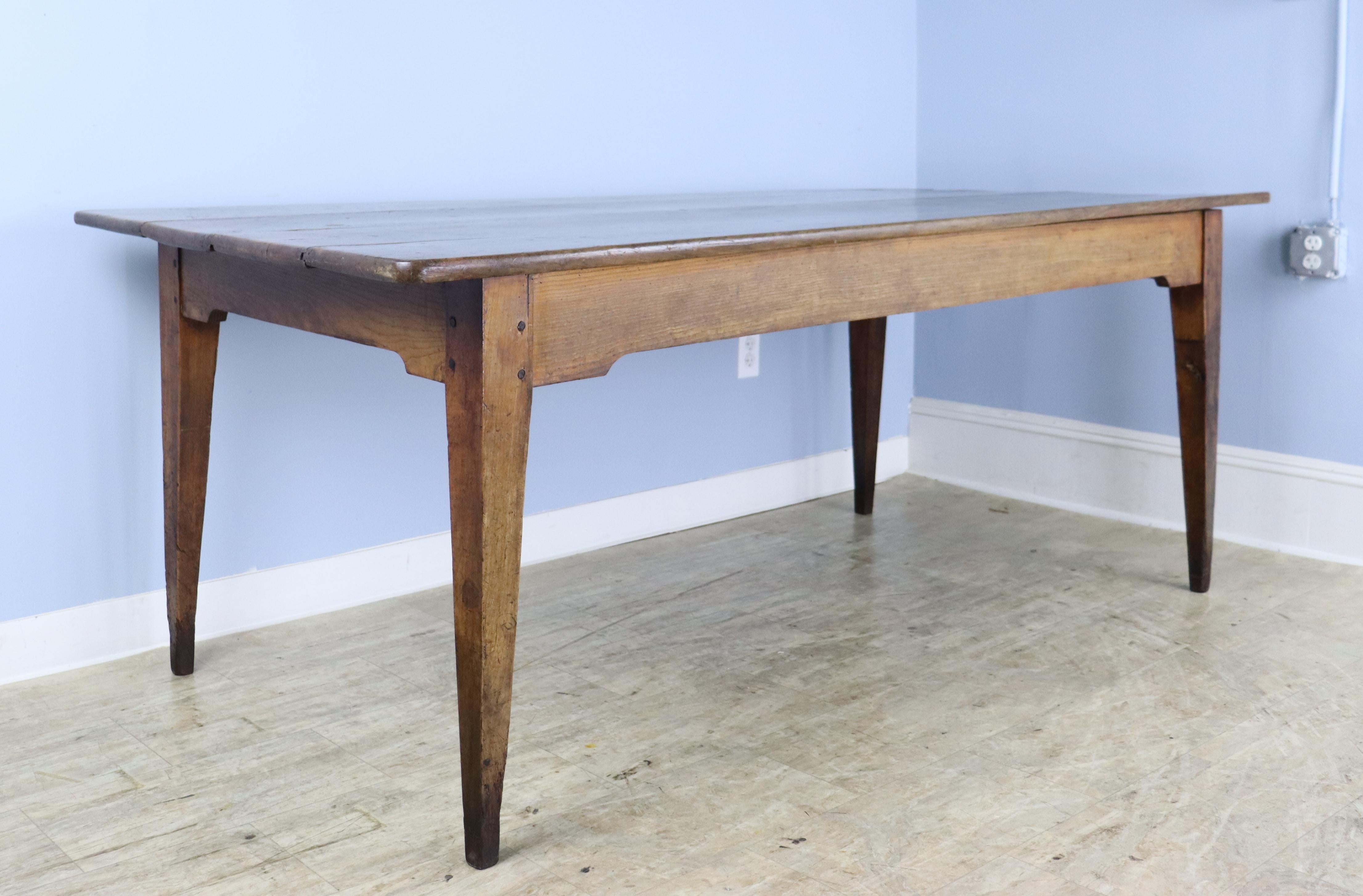 A solid country farm table in warm cherry. The wood has very nice grain, patina and color, and the table's charming drawers and carved apron add an eye catching design note. Classic tapered legs, well pegged at the base. There are some small areas