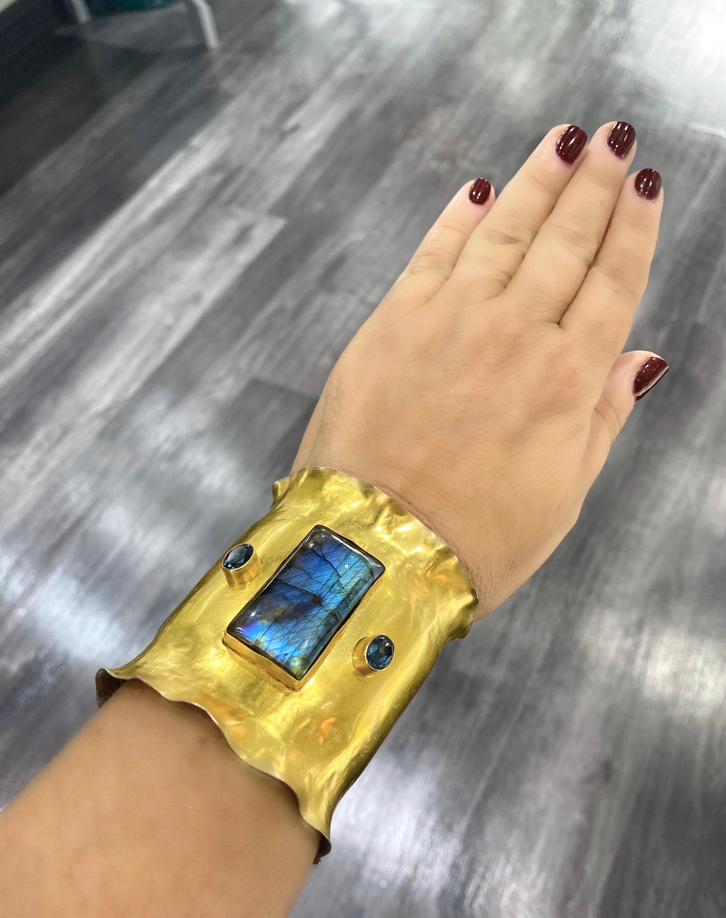 The Bijoux De Mer signature Ruffle Cuff is handcrafted with a stunning large labradorite, 65 ct, and faceted London blue topaz, bezel-set in 18k yellow gold.  The cuff itself is made of 22k gold bi-metal for durability and contrast- a sheet of 22k