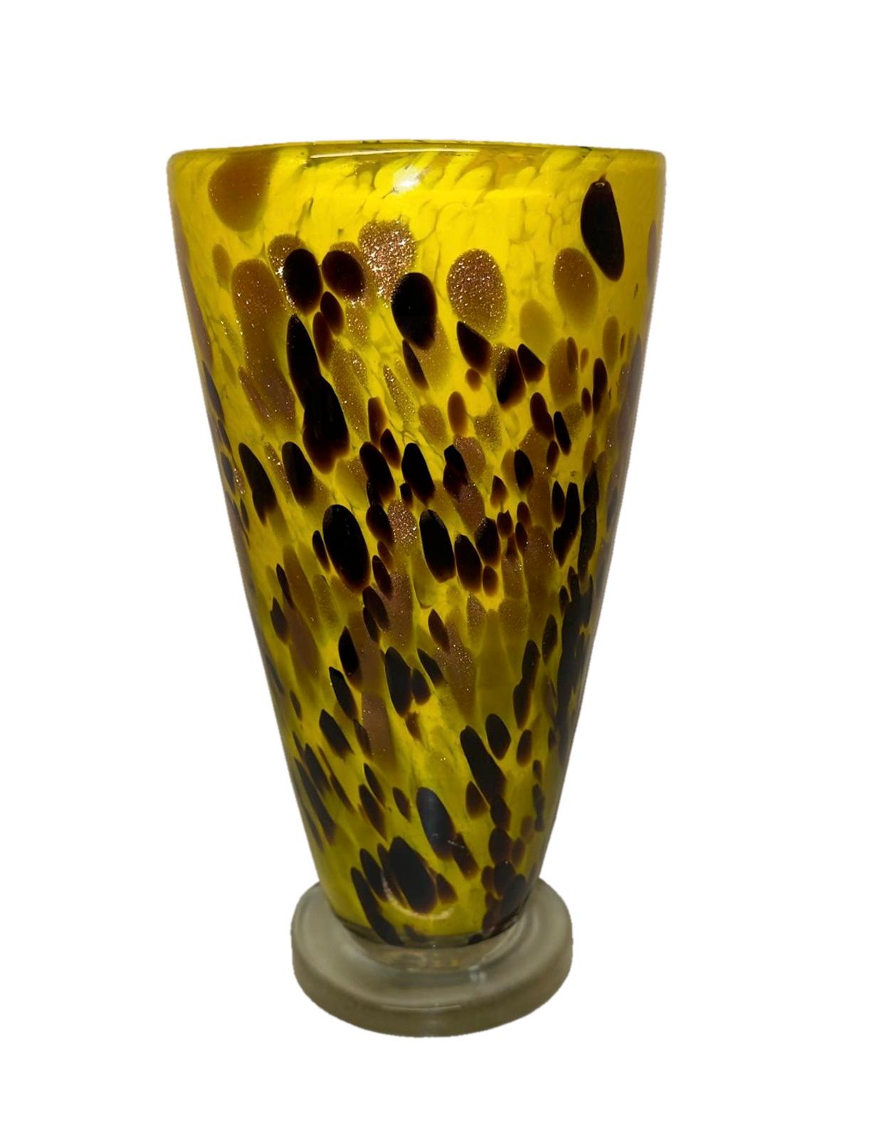 Diese lebendige und ausdrucksstarke Vase aus mundgeblasenem Murano-Glas ist ein kühnes Fest venezianischer Kunstfertigkeit und zeitgenössischer Farben. Der leuchtend gelbe Sockel ist mit unregelmäßigen schwarzen und bernsteinfarbenen Sprenkeln