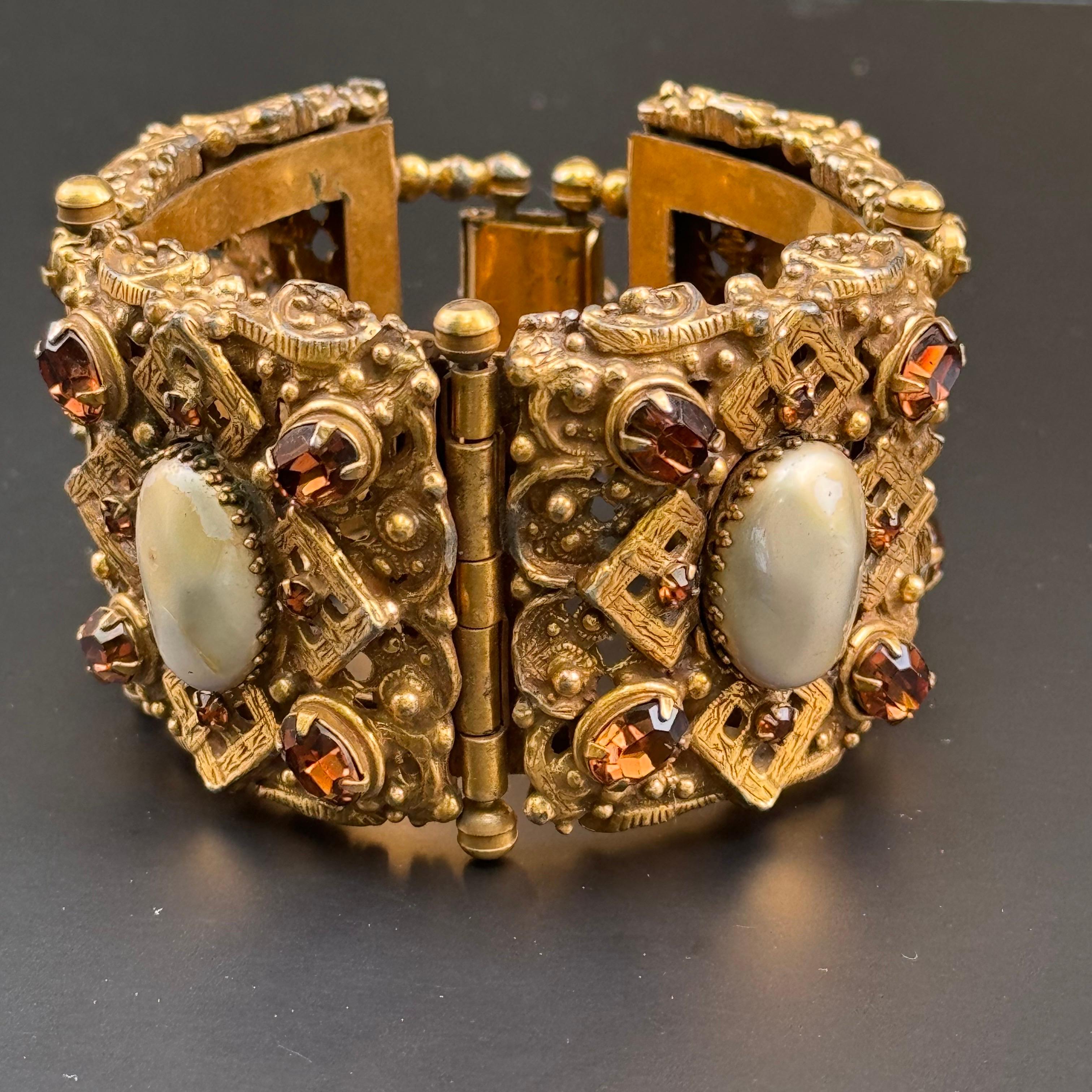Prova il lusso di un braccialetto vintage finemente lavorato con questo splendido pezzo. Questo ampio braccialetto placcato oro presenta intricati pannelli traforati ornati da finte gemme incastonate e finte perle mabe, che emanano eleganza e