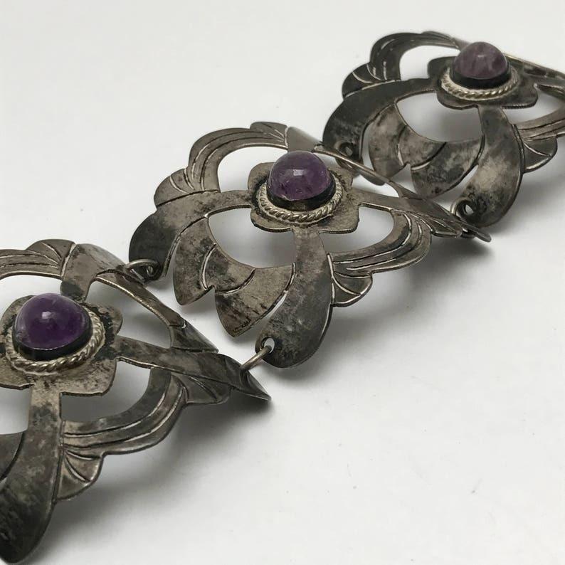 A beautifully crafted vintage Mexican sterling silver bracelet, featuring hand-wrought openwork panels each set with a cabochon amethyst at the center. This bracelet is an exemplary piece of mid-20th-century Mexican silversmithing, showcasing both