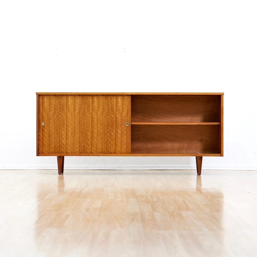 Porzellanschrank aus der Mitte des Jahrhunderts, hergestellt in England in den 1970er Jahren.  Der schlichte, breite Schrank aus edlem Mahagoni verfügt über zwei Schiebetüren mit Messinggriffen, hinter denen sich Ablagefächer verbergen.  Er steht