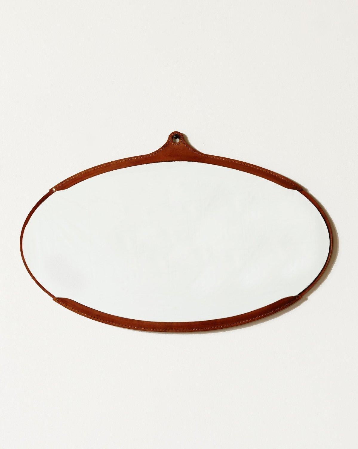 Der breite ovale Fairmount-Spiegel ist ein handgenähter Lederspiegel mit einem Rahmen aus natürlichem, pflanzlich gegerbtem Leder, das mit der Zeit in der Farbe variiert und leicht nachdunkelt. Der Spiegel sitzt im Inneren des Rahmens wie eine