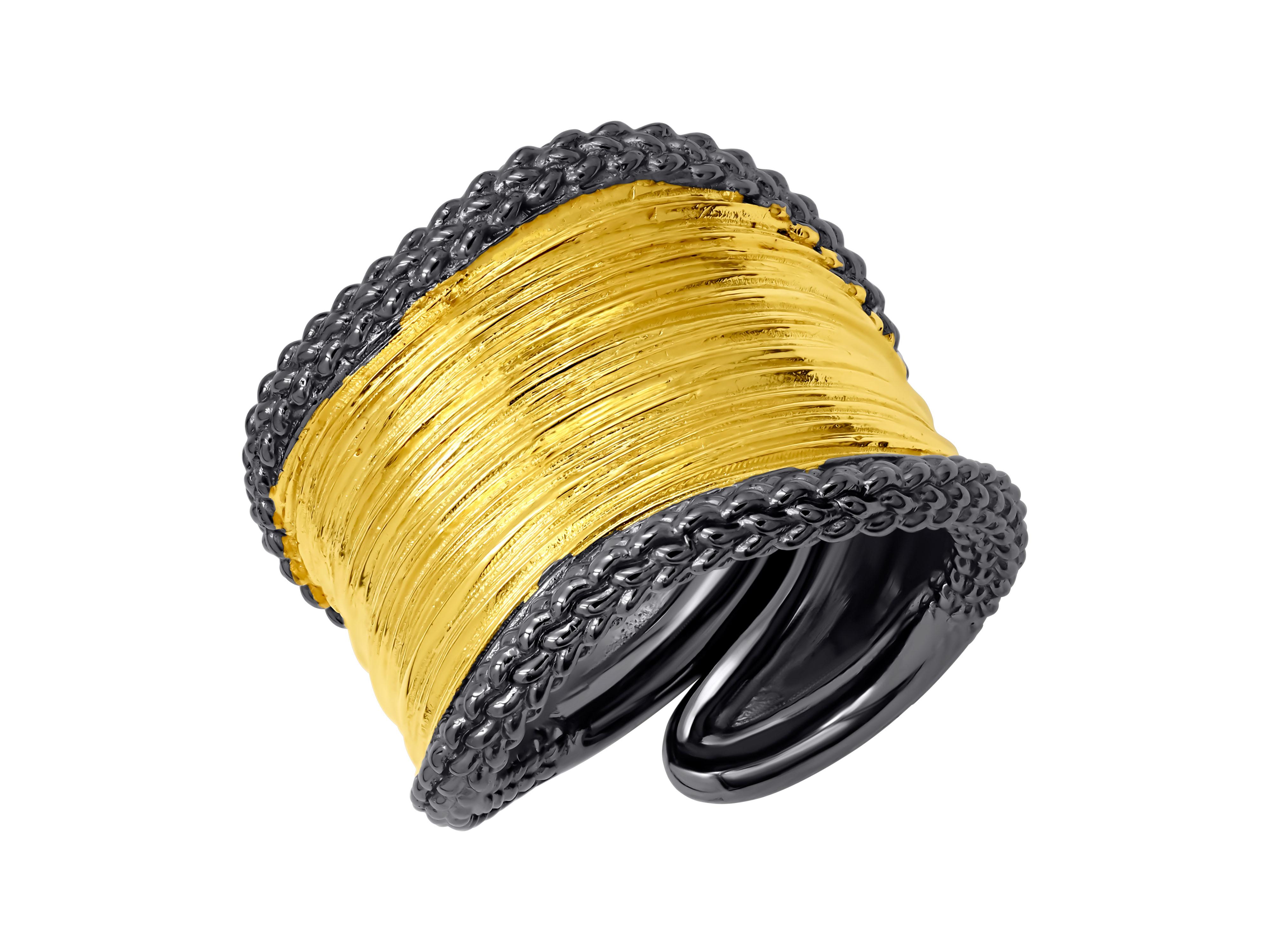 Statement piece of jewelry that features a wide band made of silver, with gold plating surface and a blackened edges. The band is adjustable and has a unique design and texture, adding an edgy and modern touch to the ring.
The gold plating gives the