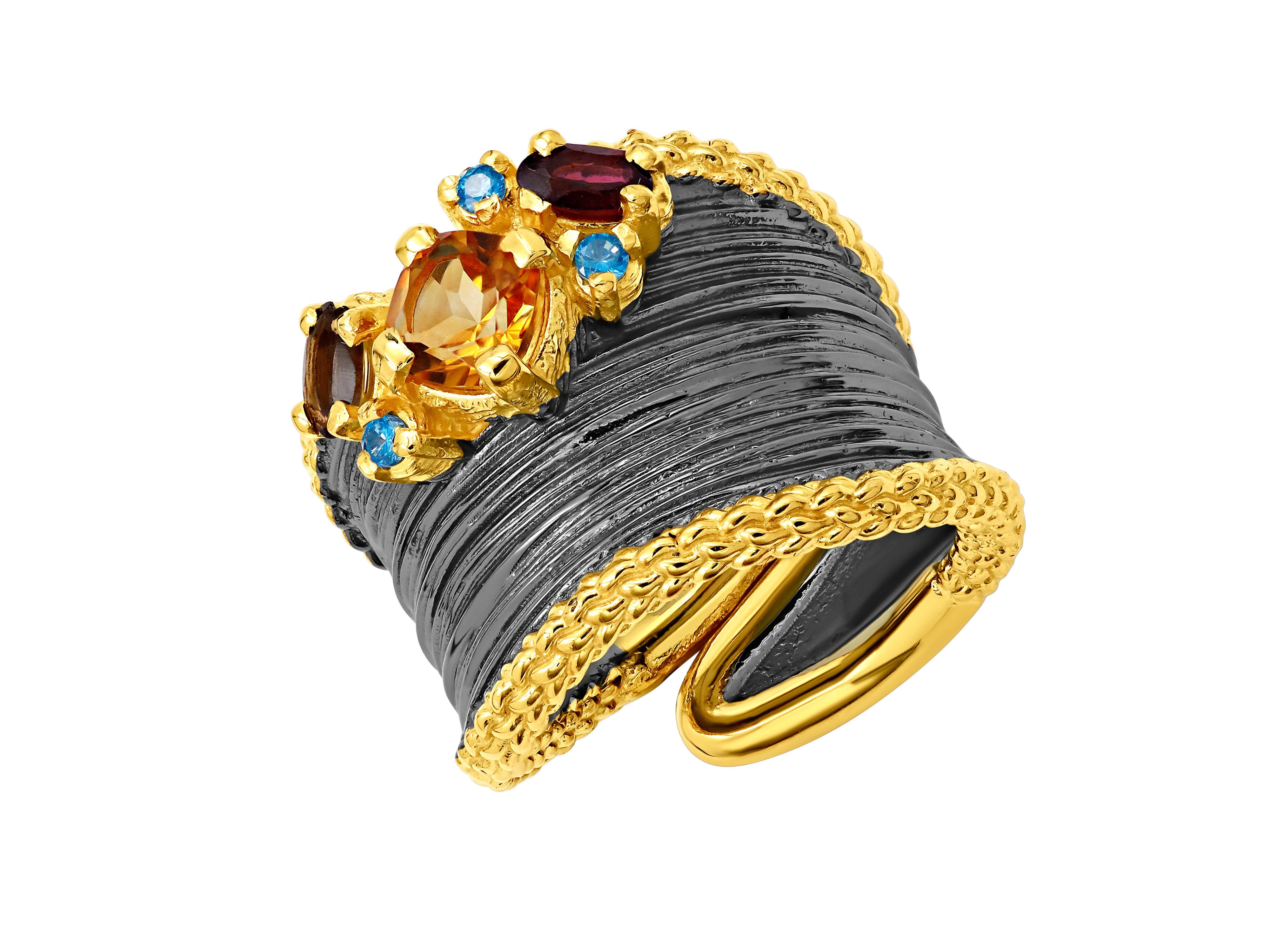 A wide silver ring adorned with vibrant gemstones: citrine, smoke, garnet, and blue topaz.
This stunning ring features a blackened, wide band crafted from sterling silver, elegantly wrapping around your finger. The band is slightly asymmetrical,