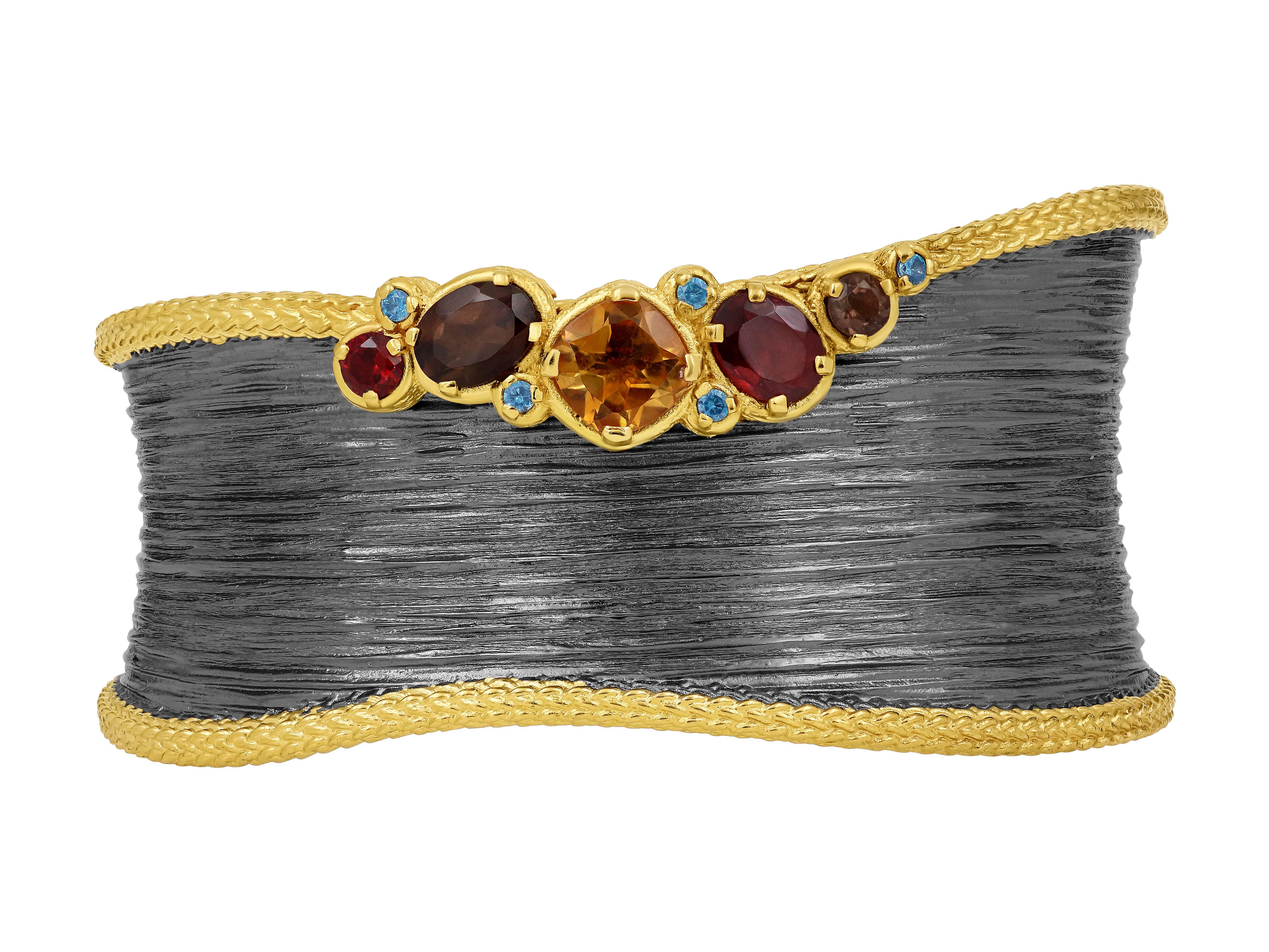 A powerful hand crafted cuff with a wonderful line texture set with citrine, smoke, blue topaz and garnets. The combination of these gemstones creates a stunning contrast, captivating the eye with its intricate and colorful design. This cuff is a