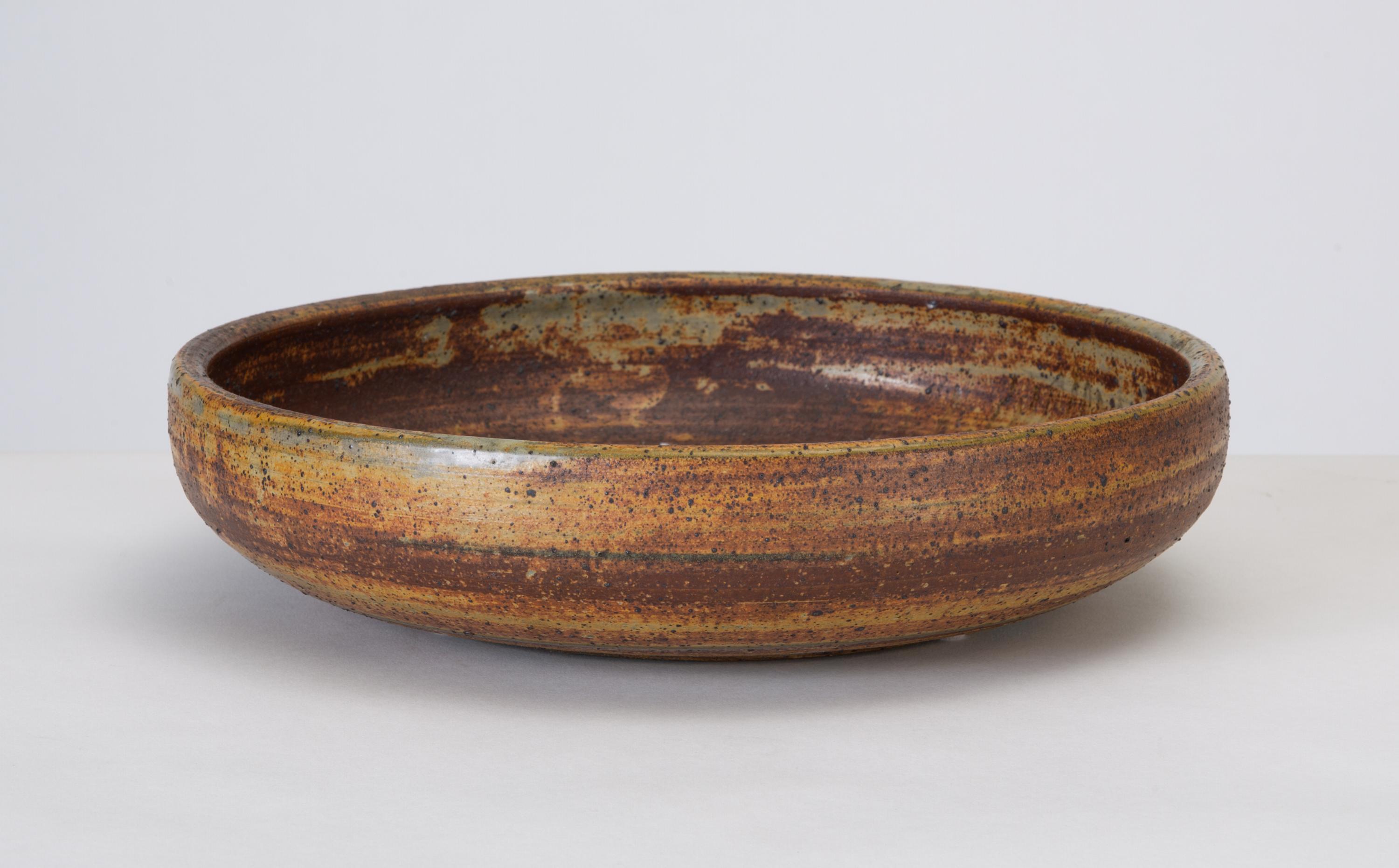 A low, wide studio pottery serving bowl in earthtone-glazed stoneware. A contrasting swirl of bright white glaze at the bottom of the dish is a focal point of the design. Signed “Beriah” on bottom. 

Condition: Beautiful vintage condition. No chips