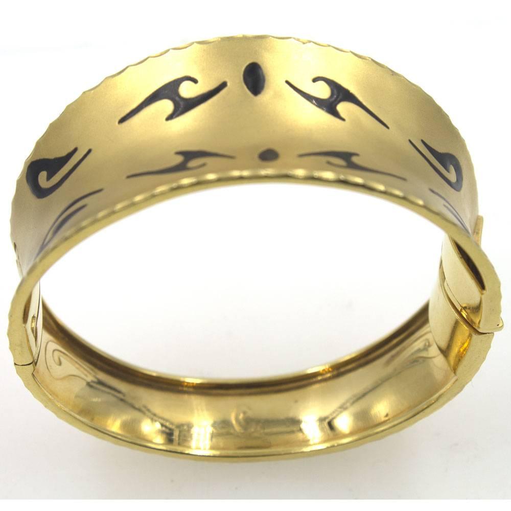 This modern tapered bangle is crafted in satin finished 14 karat yellow gold. The bangle measures .6-1.2 inches in width and approximately 7 inches in circumference. Black enamel accents add to the character of the bracelet. 