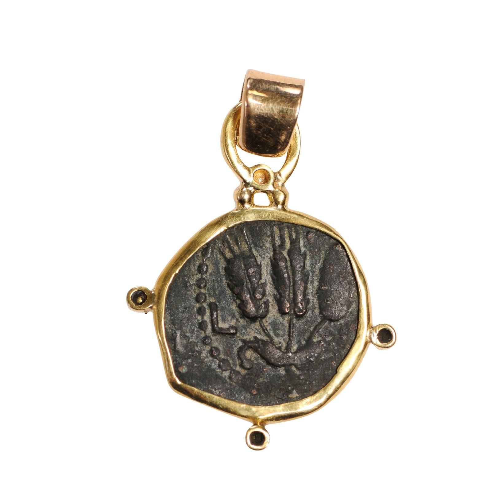 An Authentic Roman Bronze Widow's Mite Coin, Judaea, Herodians Agrippa I (37-44 AD) Prutah, Jerusalem Mint, set in a custom 22k gold bezel with 22kt gold bail. The obverse, or front, side of this coin features 3 ears of grain. On the reverse side
