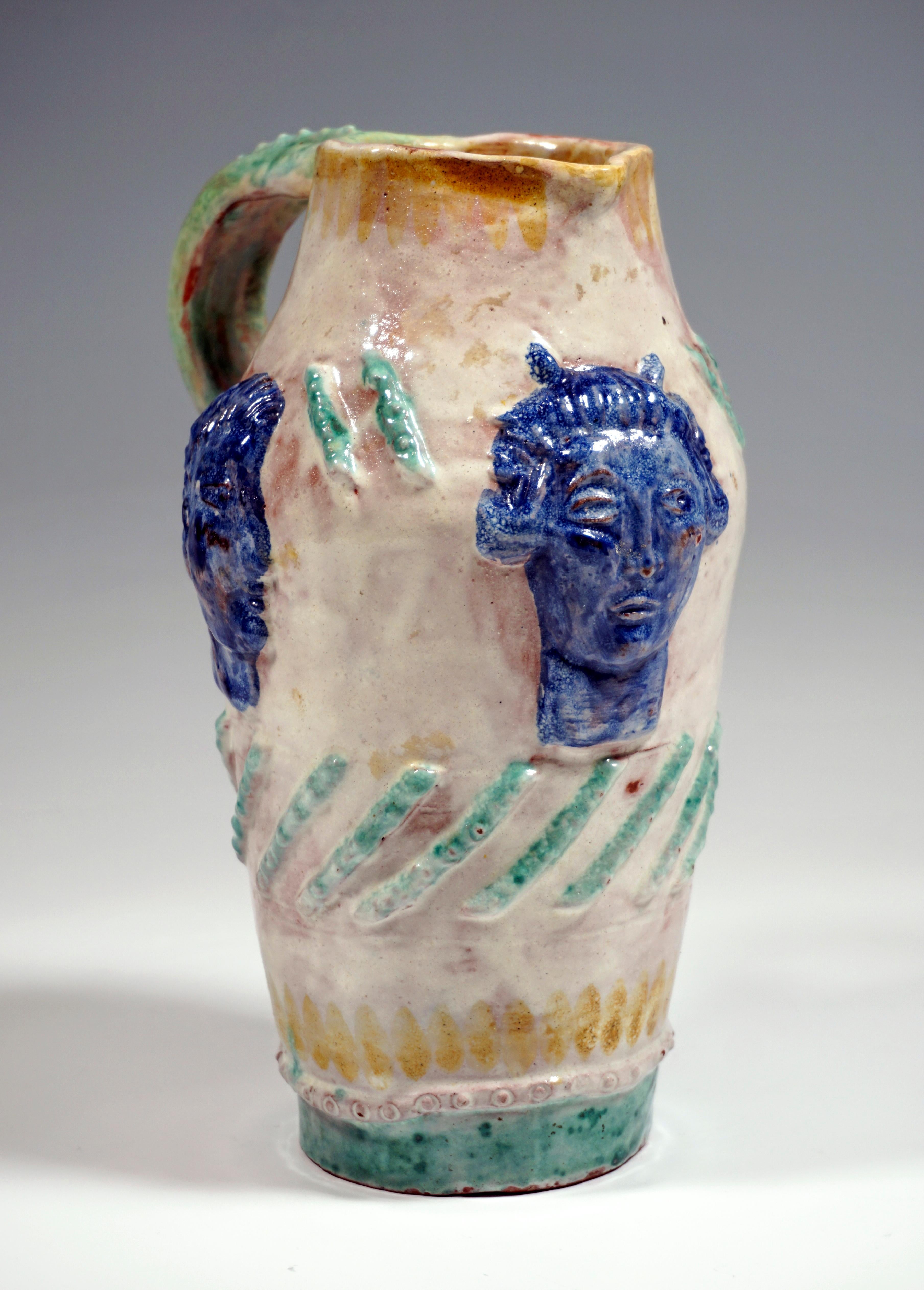 Slender jug, which widens in the upper part and narrows at the top again, with spout and opposite handle, surface decorated in relief with three antique-style heads and stylized, slanting pearl sticks, expressively colored glazed.

Manufactory: