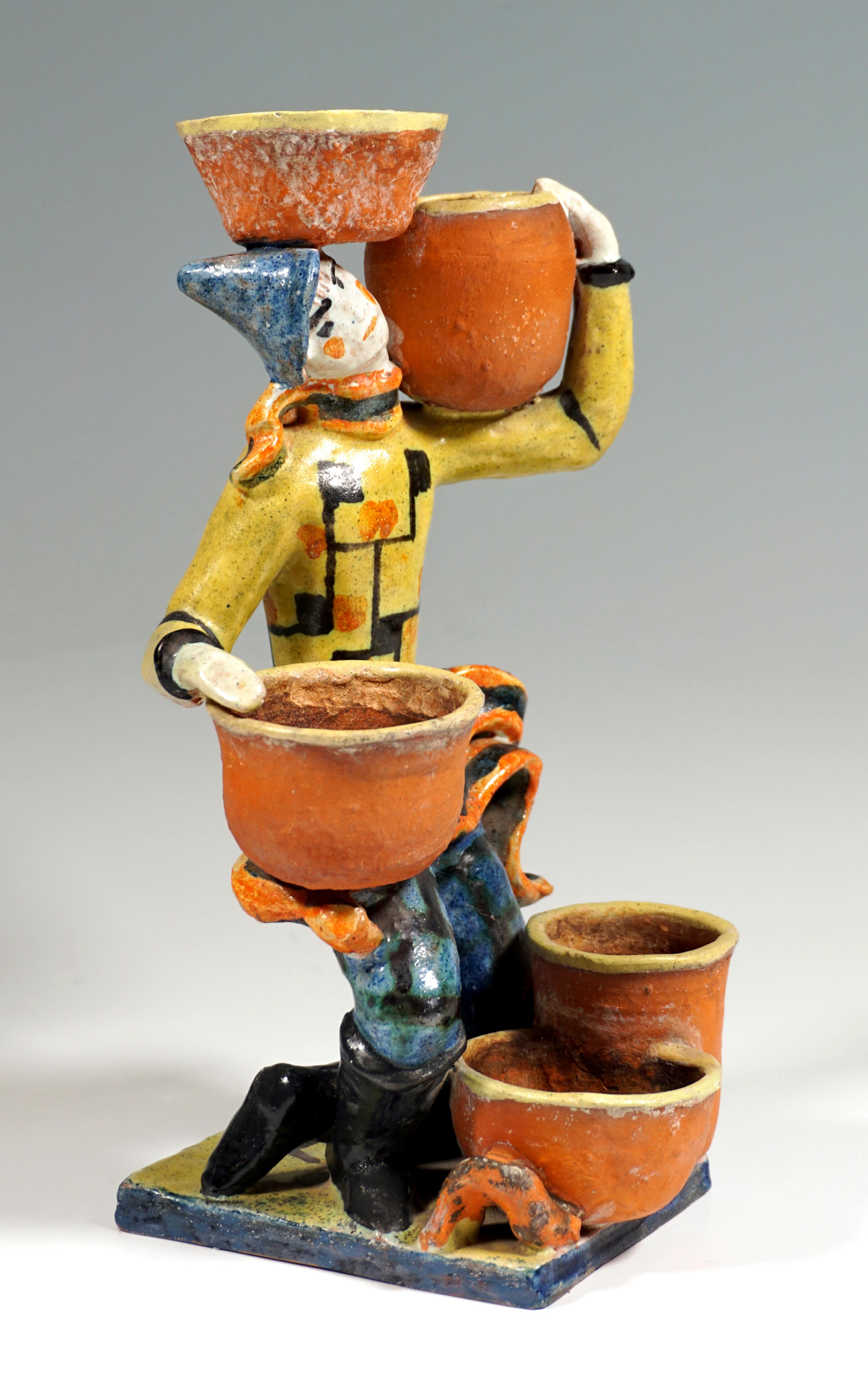 Male figure with pointed hat, kneeling on his left leg and balancing cactus pots, holding one on his left shoulder, another between it and his head, one on his right thigh, two more pots standing on the ground in front of him. On a thin, rectangular