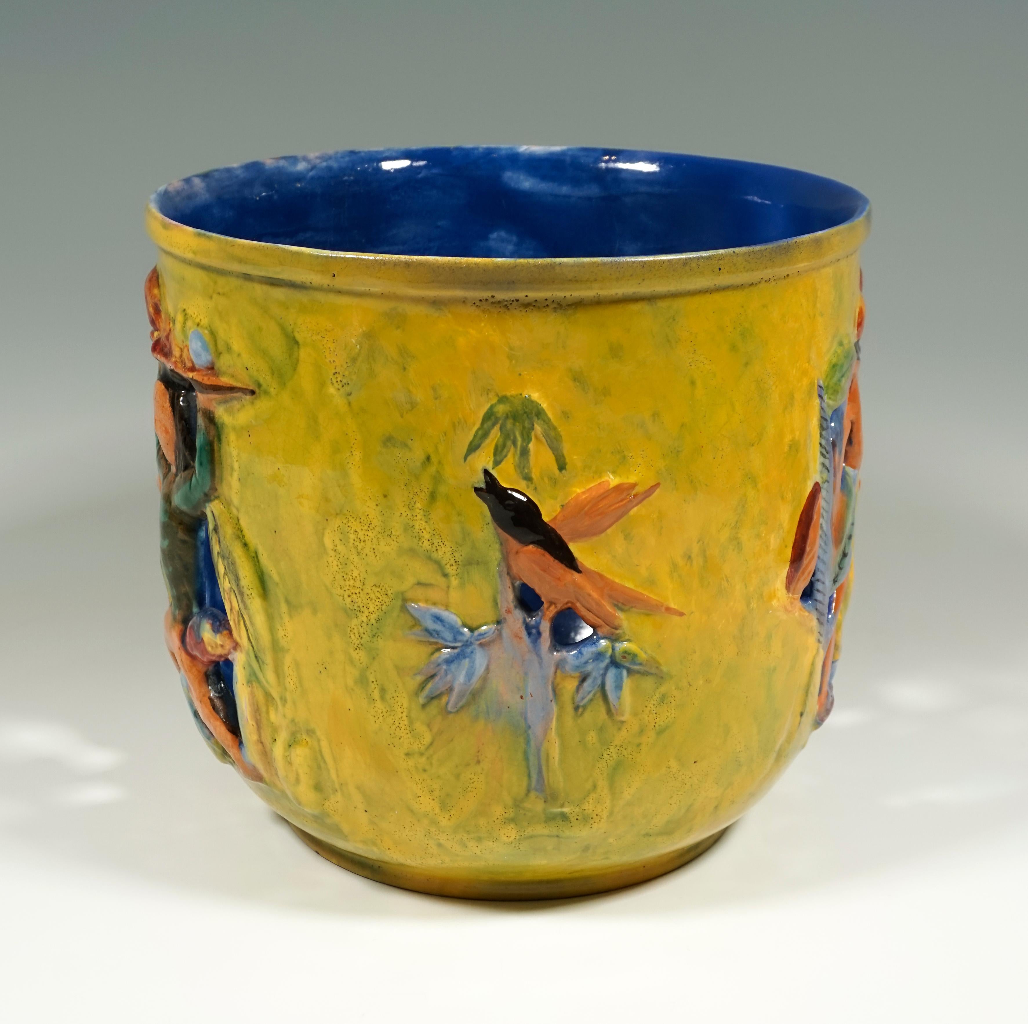 Cylindrical flower pot with breakthrough and relief-like shape of female figures carrying fruit bowls on their heads and plants with birds, painted in bright colors.

Manufactory: 'Wiener Werkstätte' /- 'Vienna Workshop'
Dating: made
