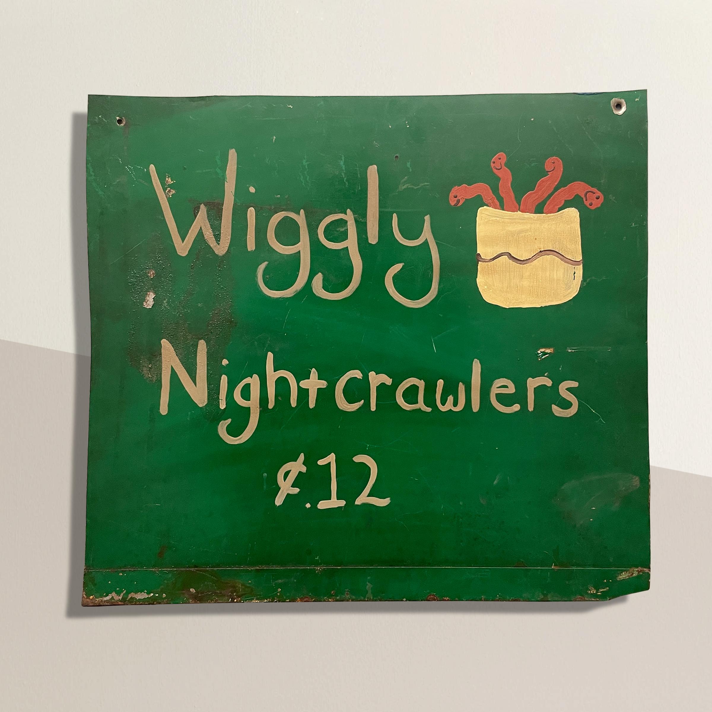 A whimsical and playful 20th century American Folk Art bait shop sign reading, 'Wiggly Nightcrawerls ¢.12' and with a jar of smiling worms crawling out of the jar. Sign comes with a custom steel wall mount that holds the sign out from the wall.
