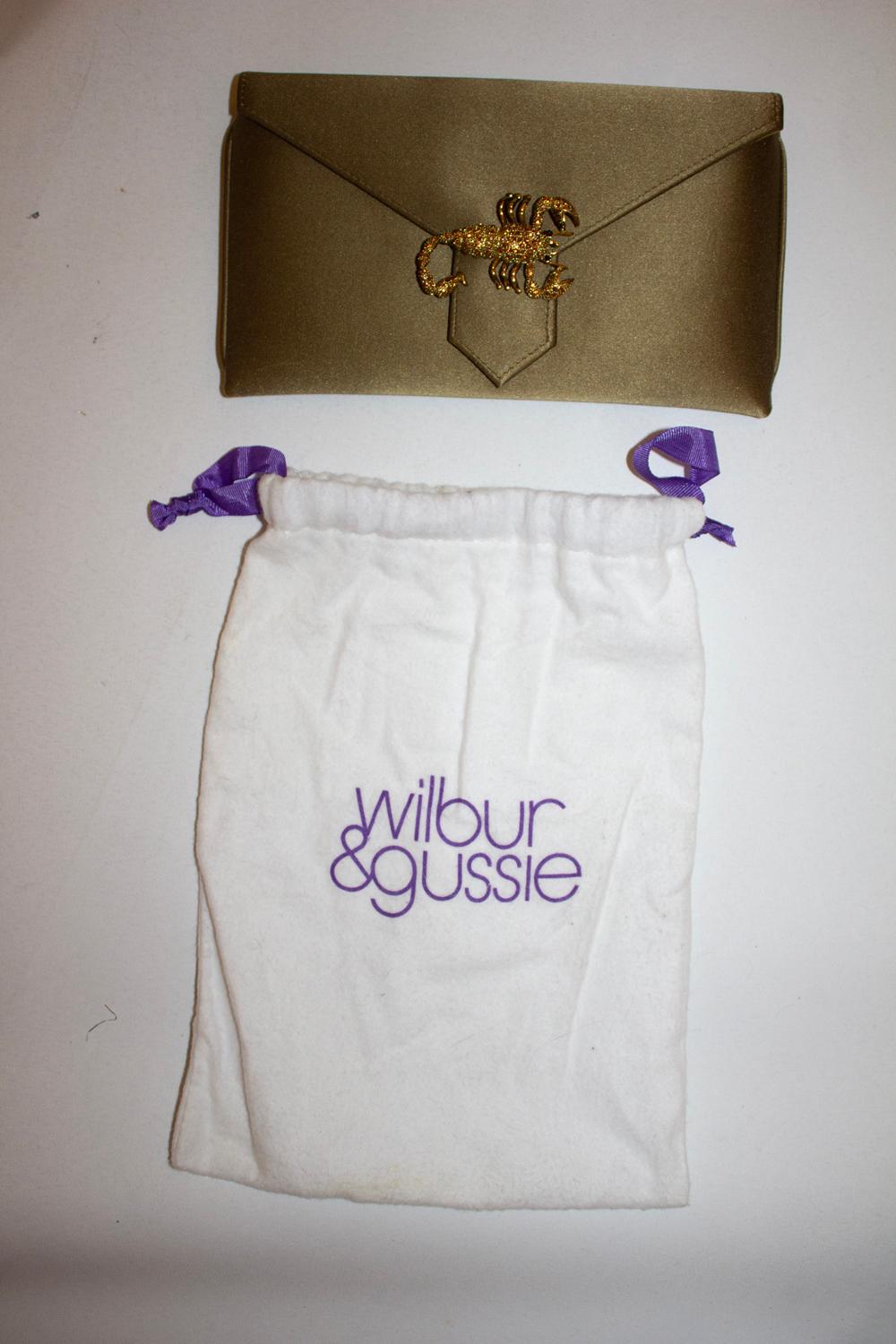 Eine schicke und witzige Abendtasche von Wilbour und Gussie. Die Tasche ist aus einem attraktiven olivgrünen Seidensatin und hat einen Druckknopfverschluss.  Sie hat eine Innentasche und eine verdeckbare Handschlaufe. Die Tasche hat ein attraktives