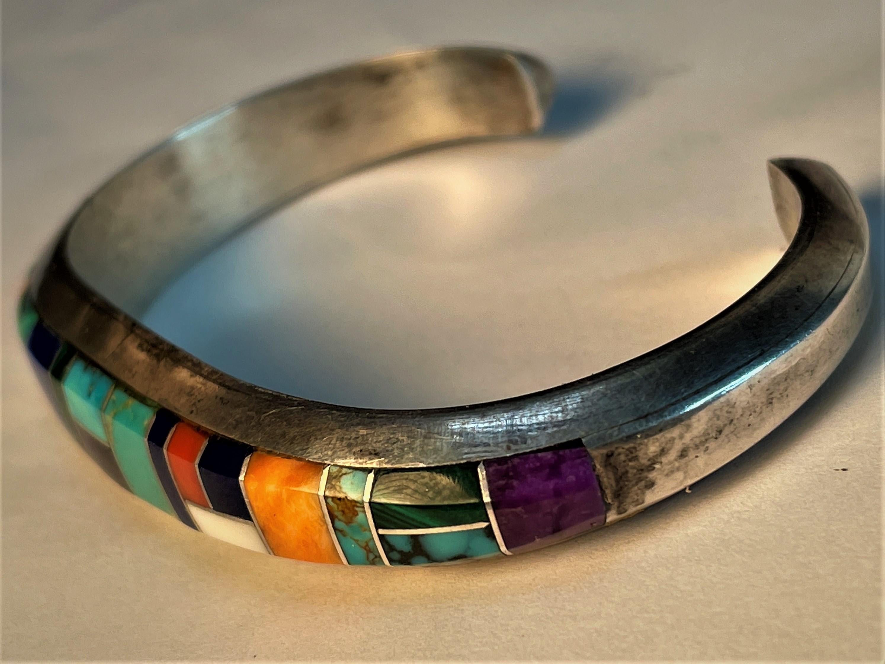 This is a fine quality Navajo sterling silver cuff bracelet with various gemstones in different shapes and sizes inlaid in a pleasing pattern on the front of a heavy nicely shaped cuff bracelet made by Wilbur Musket and signed W.M. Sterling on the