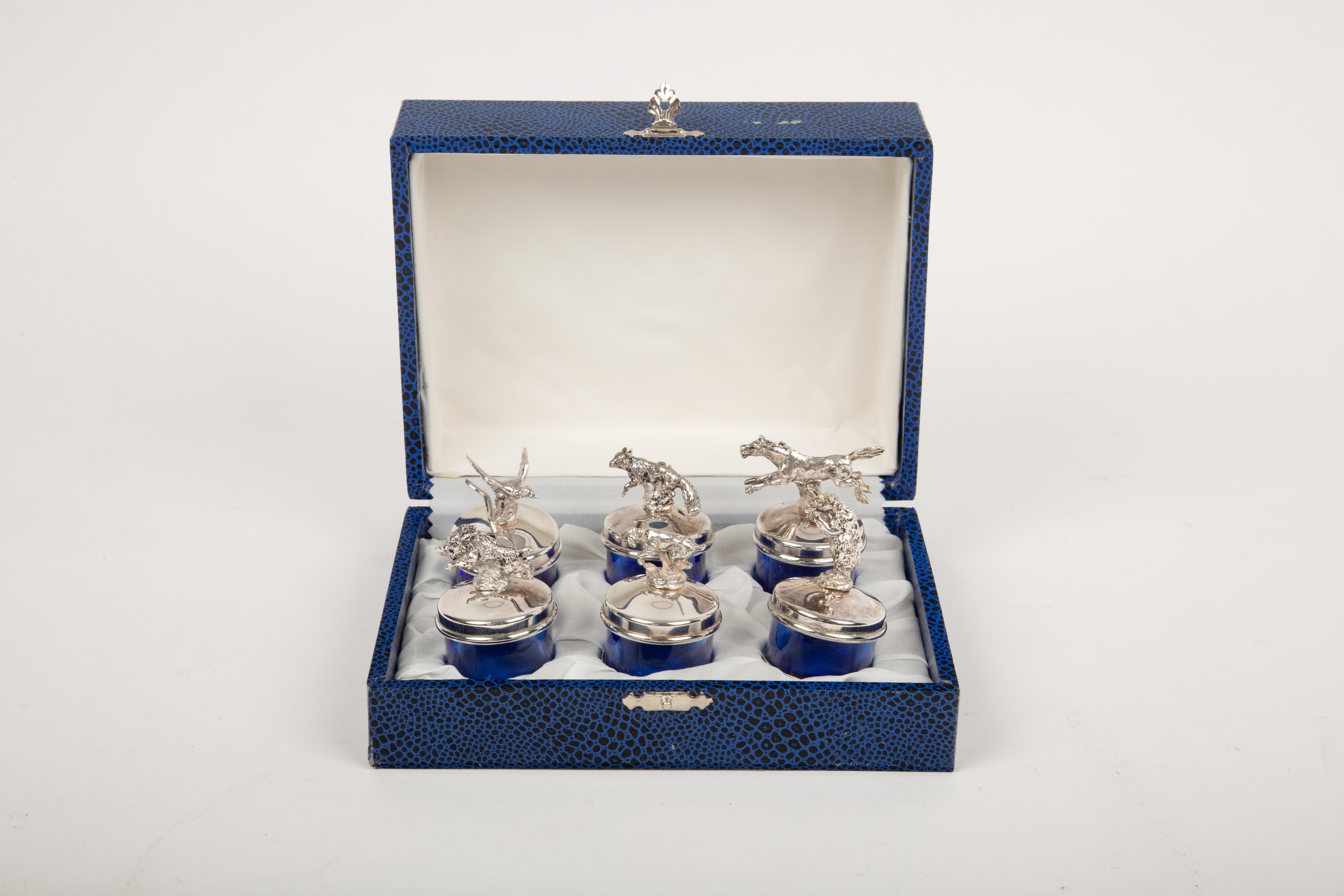 Este elegante juego incluye seis saleros de cristal azul cobalto, cada uno de ellos con una tapa de metal plateado adornada con intrincados y detallados motivos de caza, que sirven también como portavasos. Los animales representados -pato, jabalí,