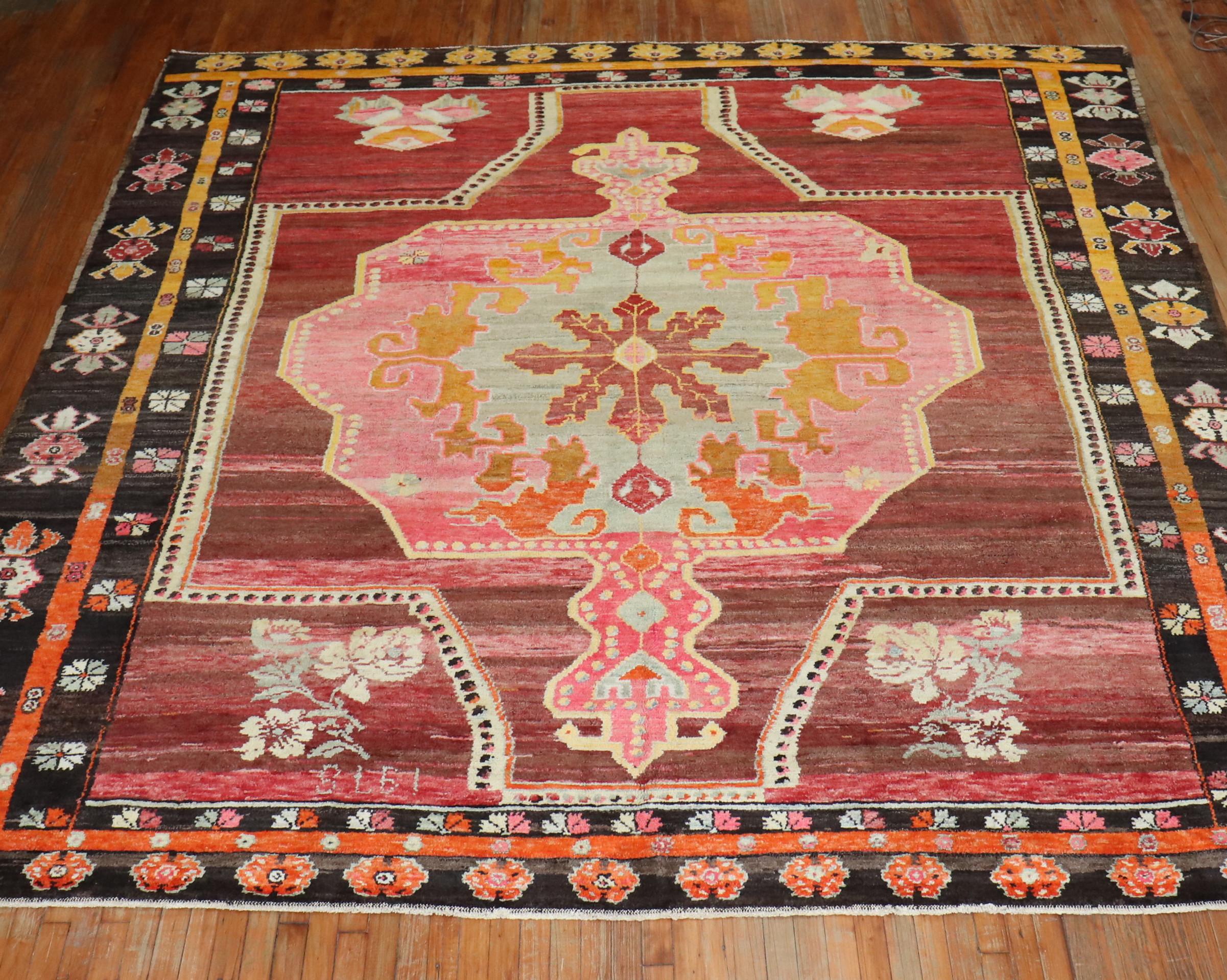 A wild 20th century Turkish Kars square size rug. A large scale floral design featuring a bright pink medallion with a striated brown and soft red field, 4 floral bouquets in the field surrounded by a multi-band border in brown and orange. Border.