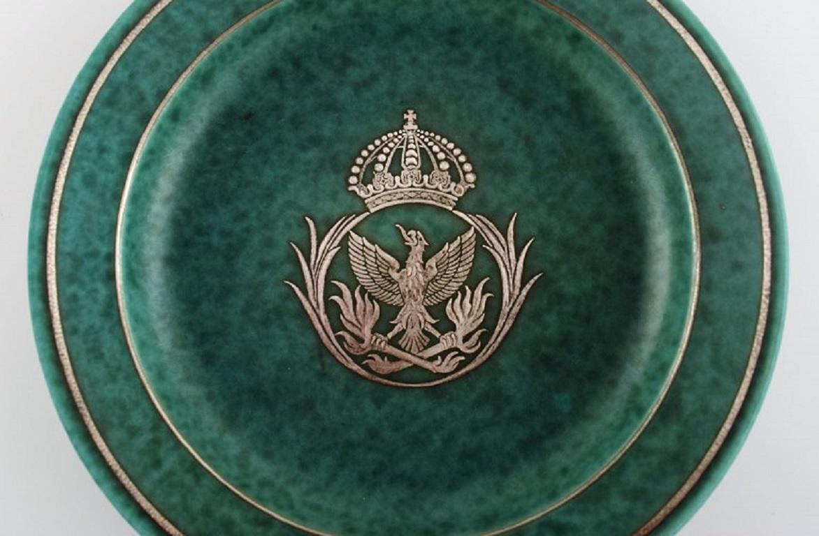 Wilhelm Kåge (1889-1960) for Gustavsberg. 
Argenta Art Deco dish in glazed ceramics. Beautiful glaze in shades of green with silver inlay in the shape of an eagle and a royal crown. 
Mid-20th century.
Measures: 23.5 x 4 cm.
In excellent