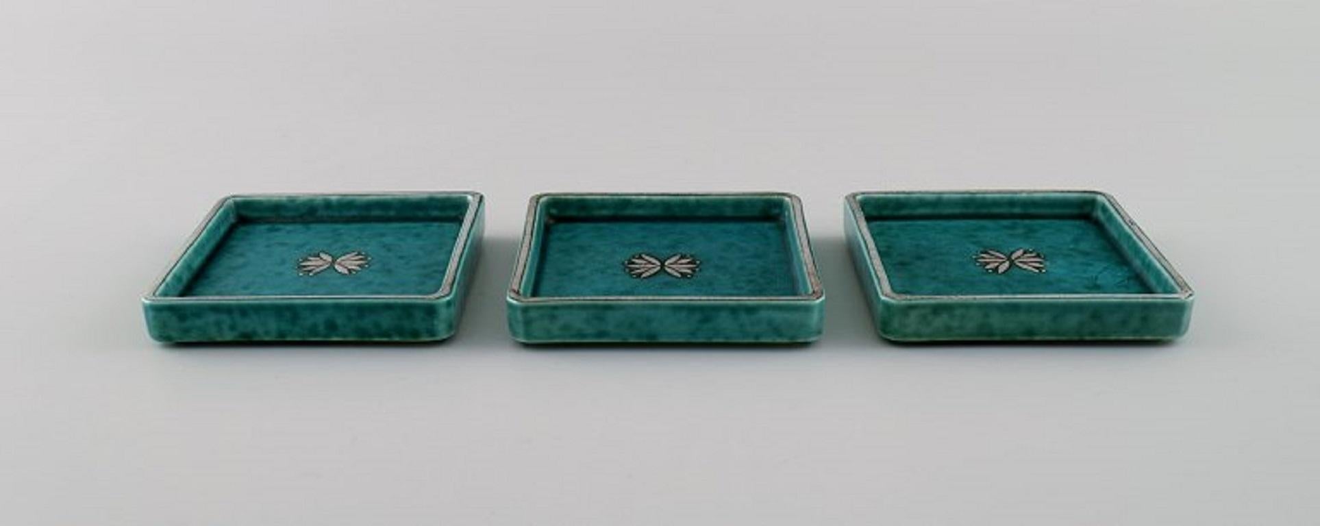 Wilhelm Kåge (1889-1960) for Gustavsberg. 
Three Argenta Art Deco dishes in glazed ceramics. 
Beautiful glaze in shades of green with silver inlay. 1940s.
Measures: 9 x 9 x 1.6 cm.
In excellent condition.
Stamped.