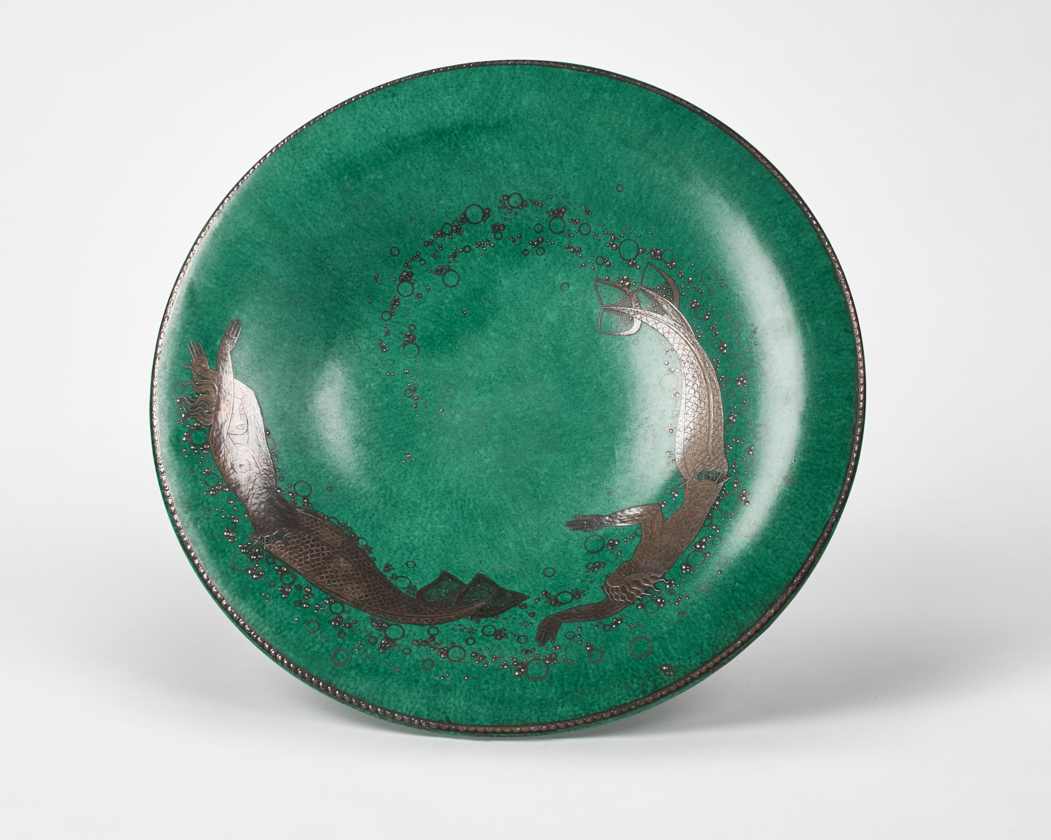 This beautiful piece is part of the artist's Argenta Series, produced for the Gustavsberg Factory, which first won him major success. The series includes everything from ashtrays to 60 kg urns-- primarily in a green glaze with silver details, circa